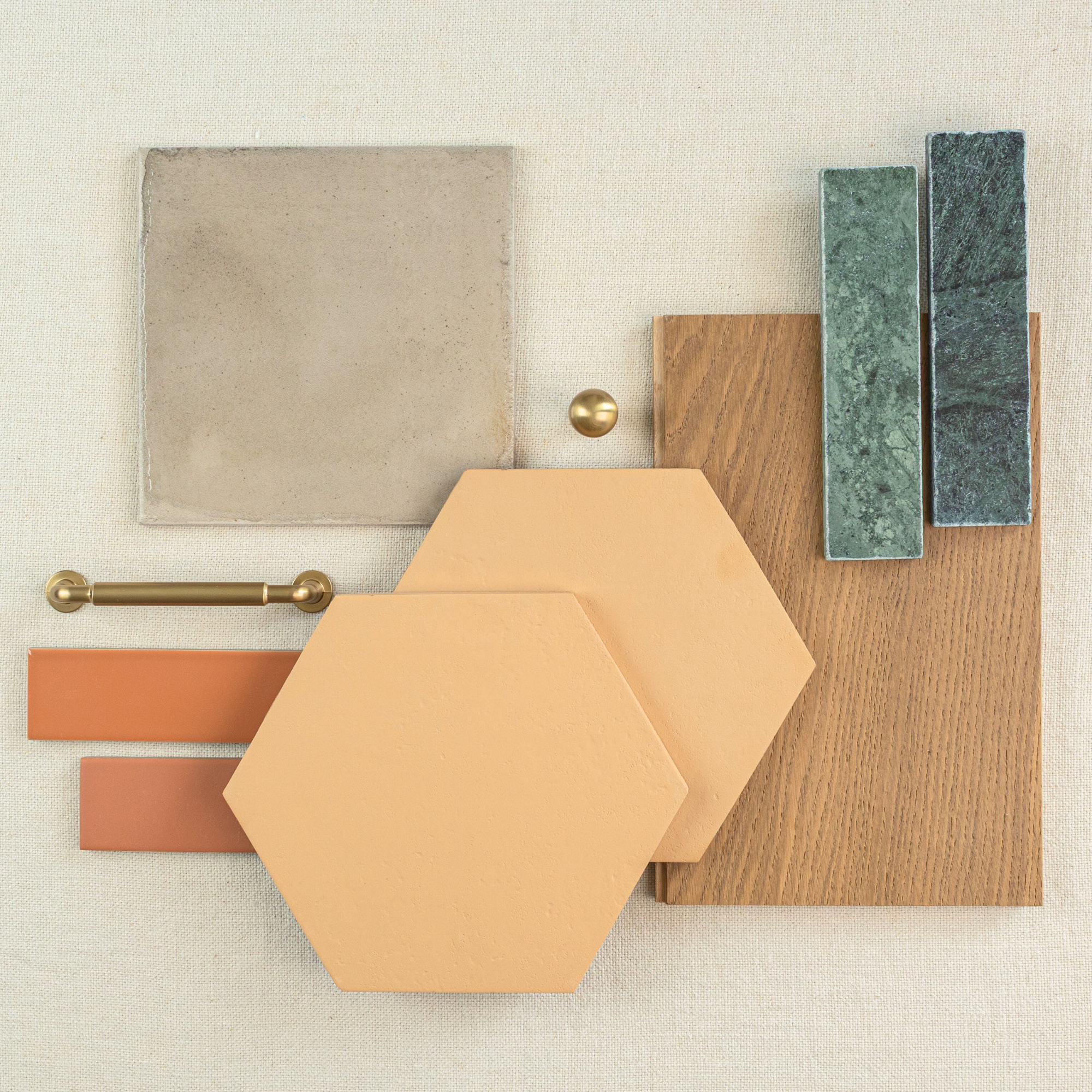 Flat lay of hexagonal terracotta tiles, wood plank sample, green textured rectangular tiles, and brass hardware on neutral fabric background