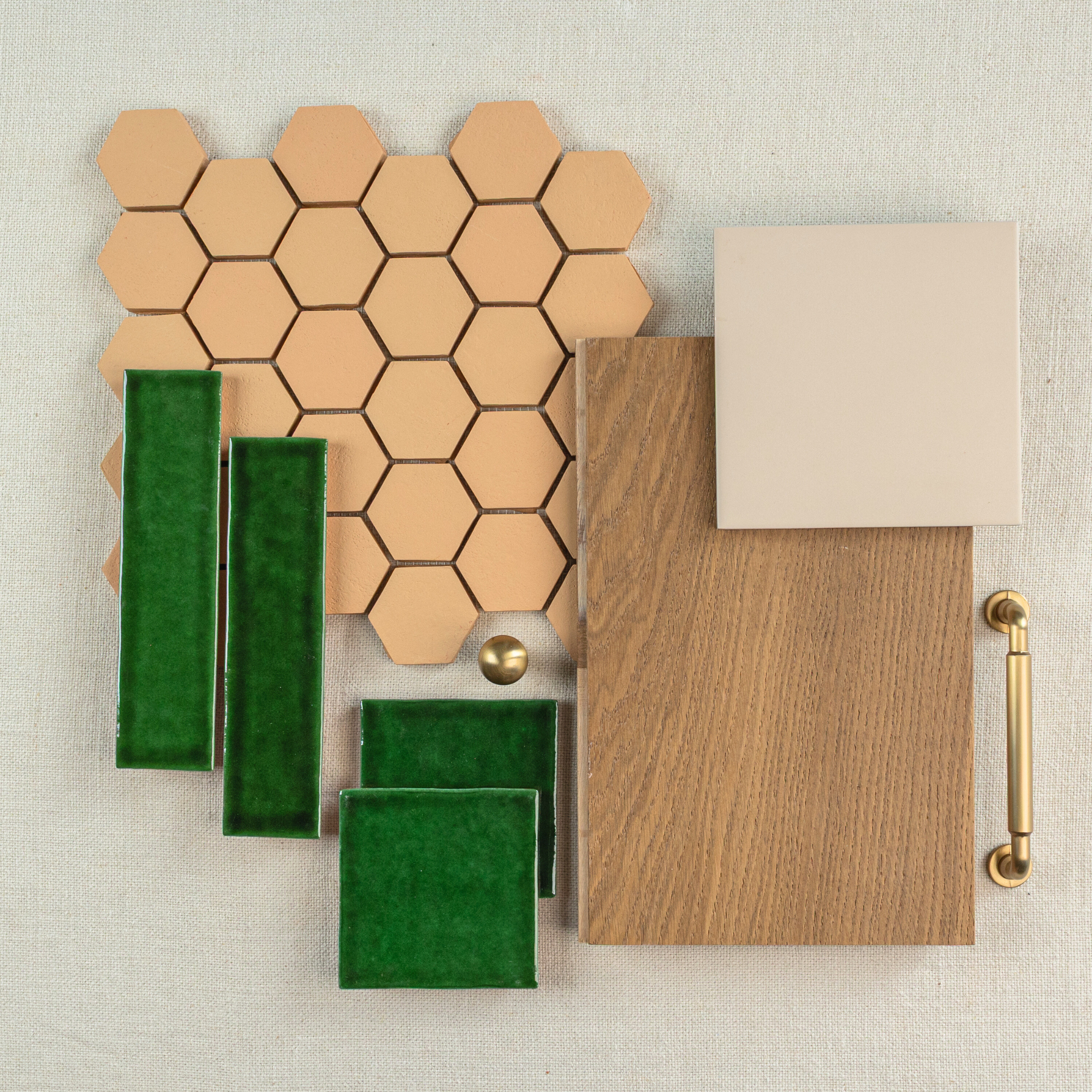 Hexagonal terracotta tiles paired with glossy green ceramic tiles, oak wood sample, beige tile, and brass hardware on light fabric background