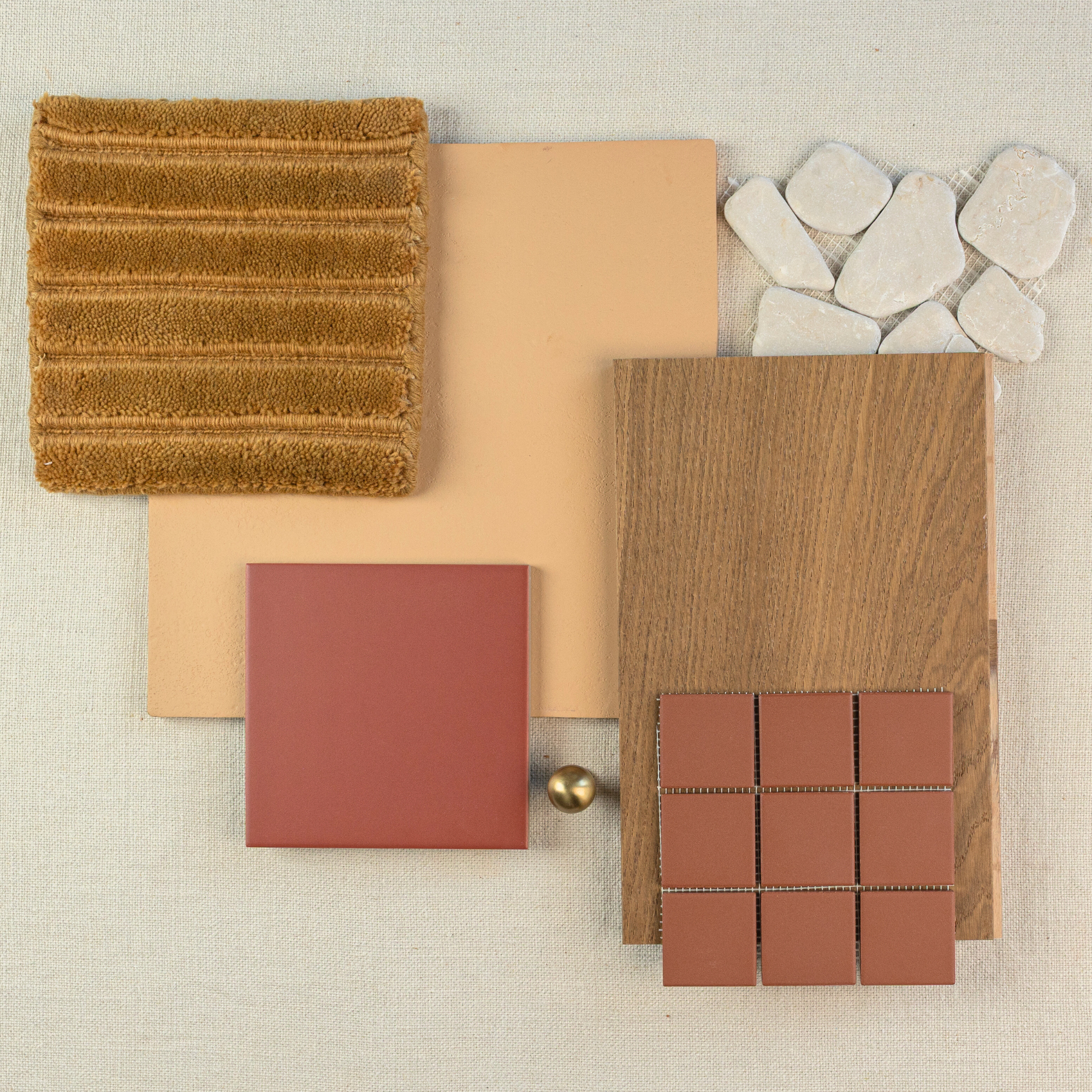 Arrangement of matte terracotta tiles, textured golden brown fabric, wood plank, small stone pieces, and brass knob on neutral surface