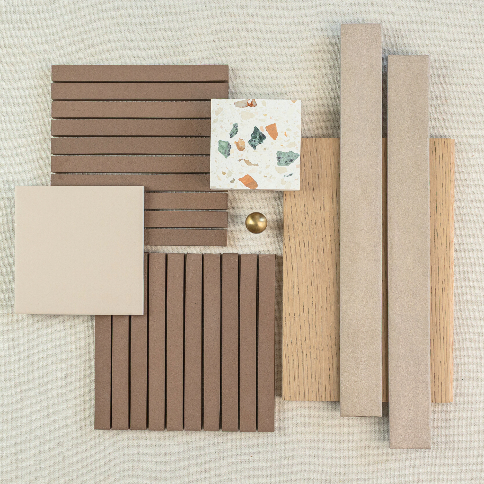 Layout of beige and brown ceramic tiles with two wood samples and a terrazzo tile on neutral fabric background