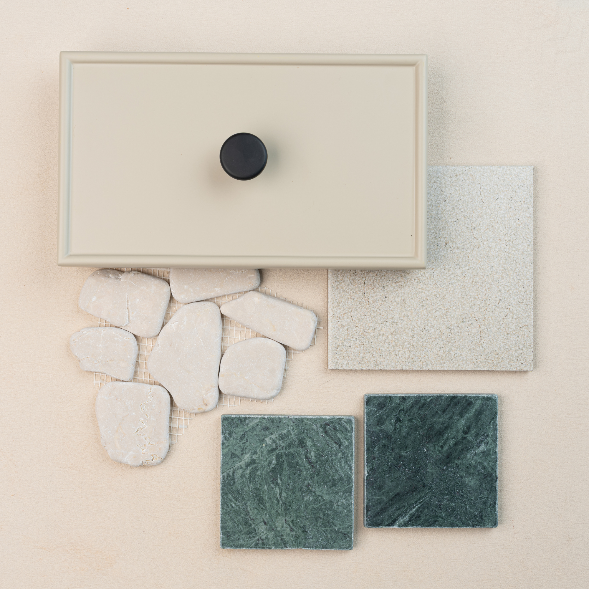 Beige cabinet drawer front with black knob above green stone tiles, light textured tile, and rough cream stone pieces on pale background