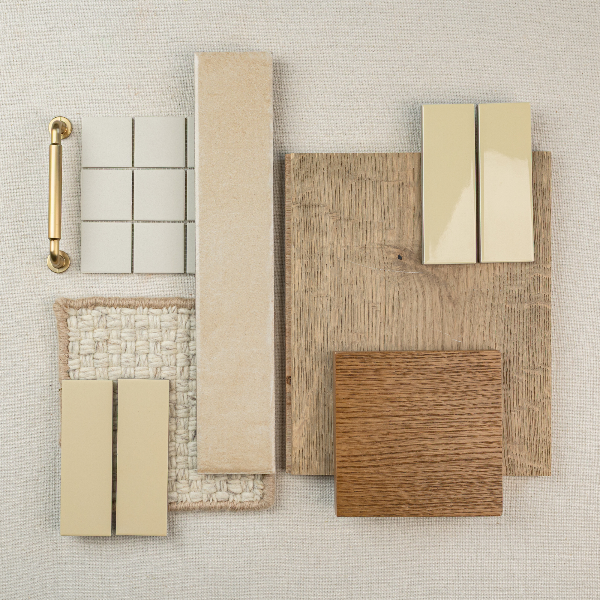 Flat lay of beige and wood tile samples, textured fabric, and a brass cabinet handle on a neutral background