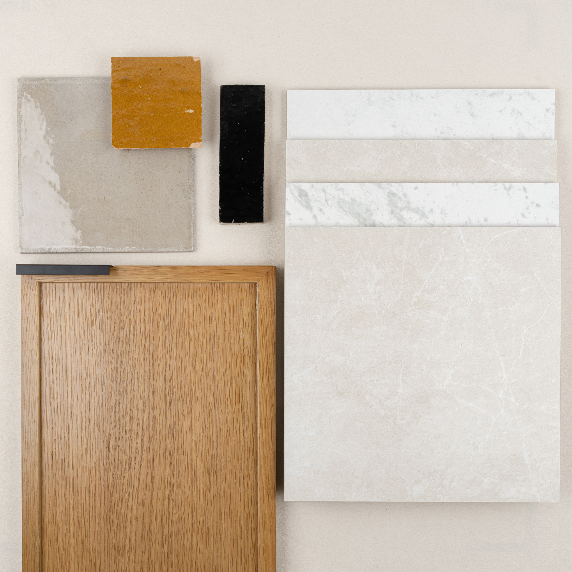Collection of neutral ceramic tiles, oak wood cabinet front, and black and amber tile samples on light background