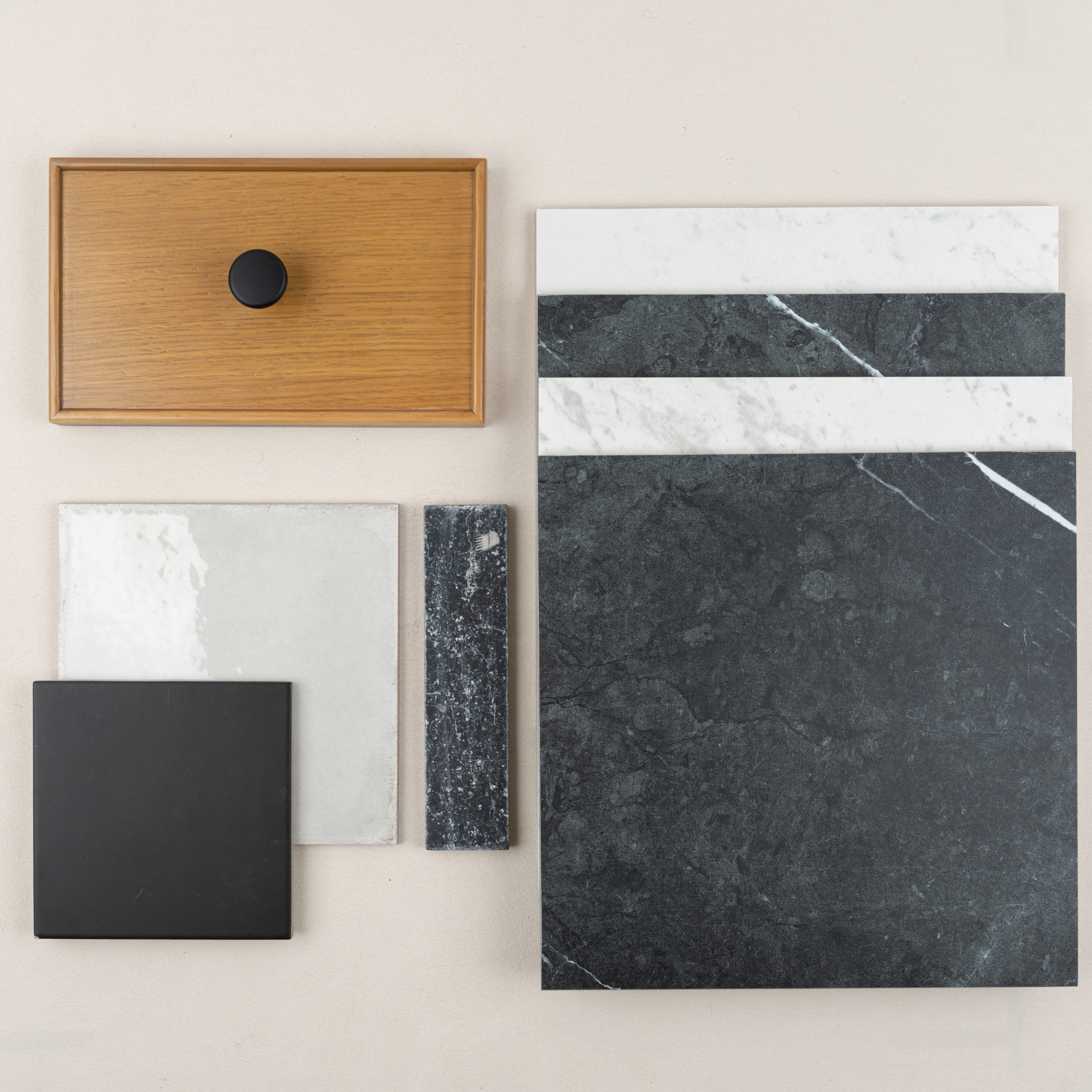 Overhead view of dark marble, white stone tiles, black ceramic tile, textured white tile, and oak wood drawer front with black knob