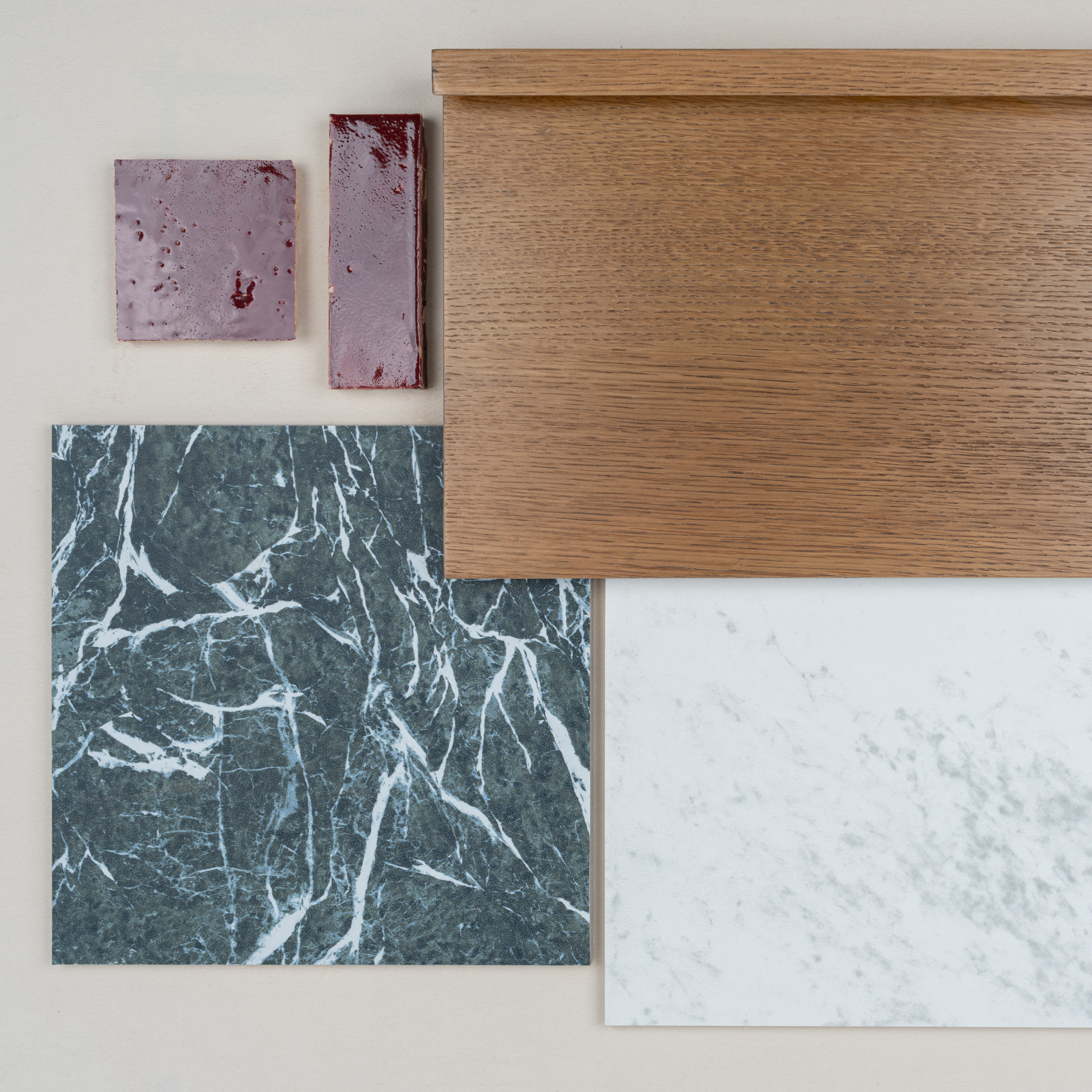 Flat lay of purple ceramic tiles, warm oak wood sample, dark green marble tile, and white marble tile on neutral background