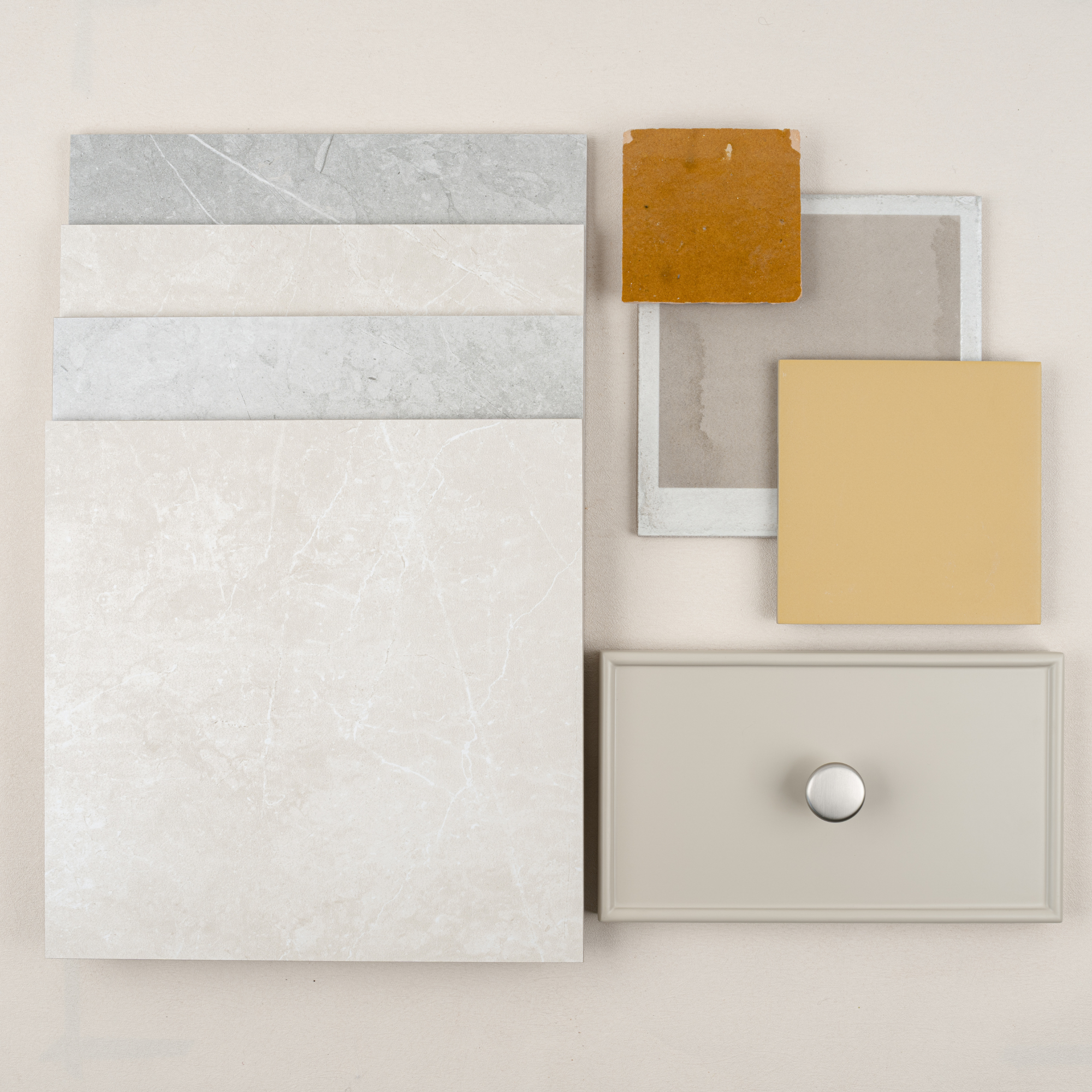 Flat lay of neutral stone tile samples paired with warm ochre ceramic tiles and a light beige drawer front with metal knob