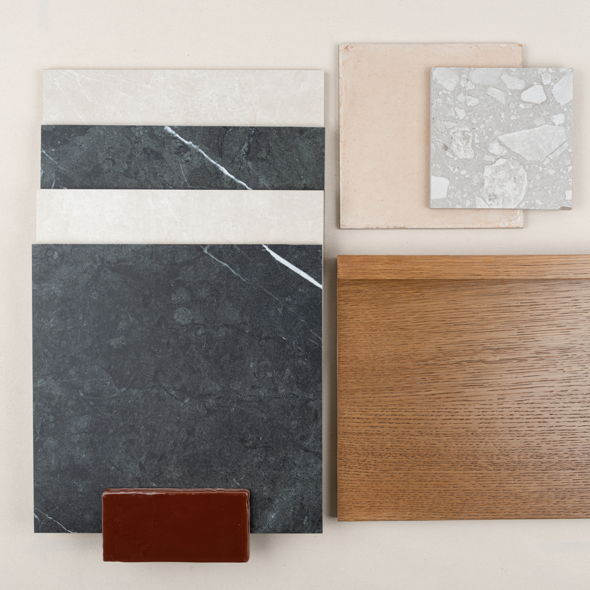 Flat lay of dark marble slabs paired with light terrazzo tiles, beige stone, warm oak wood, and a small brown ceramic tile sample