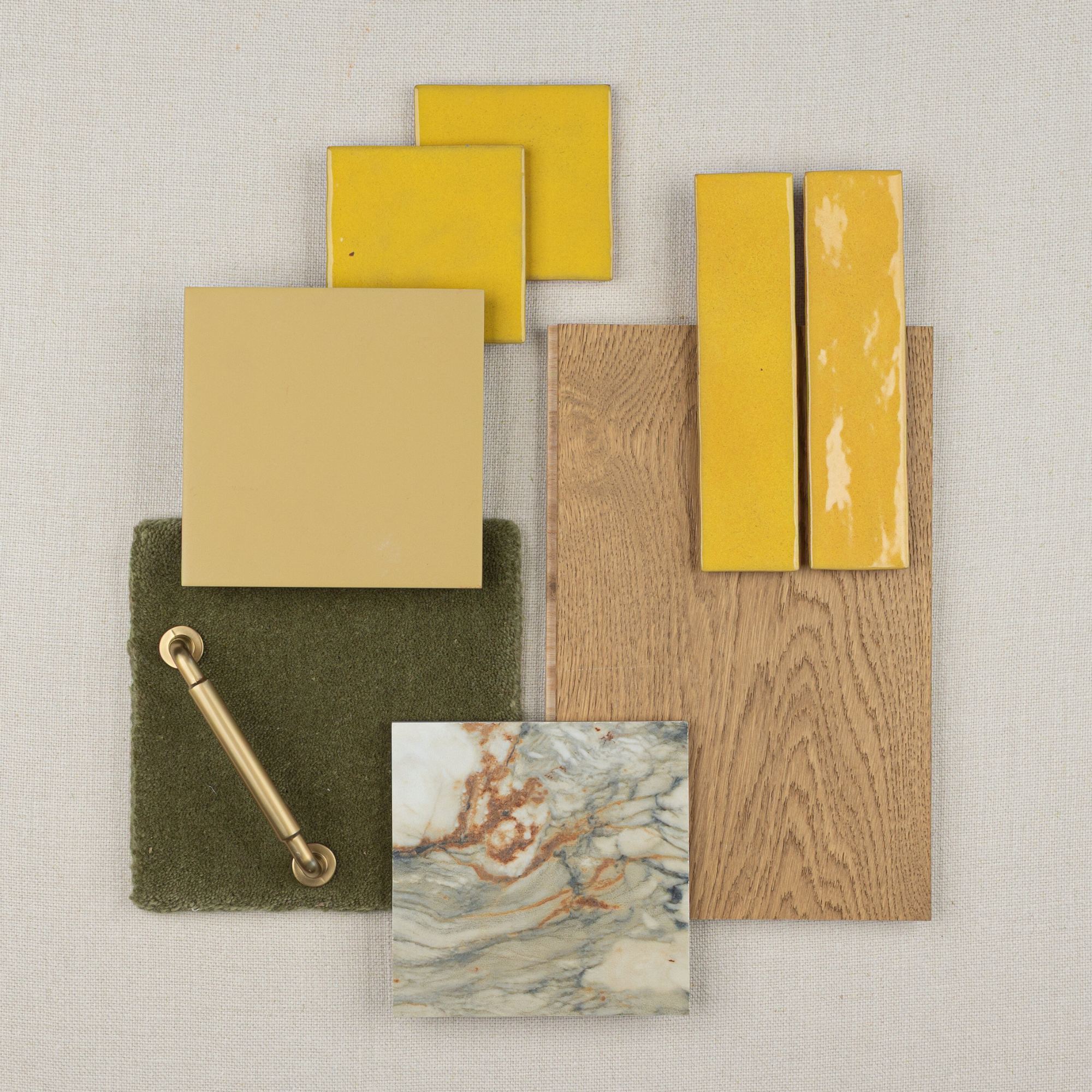 Flat lay of yellow ceramic tiles, wood sample, green fabric swatch with brass handle, and marble-look tile on light background