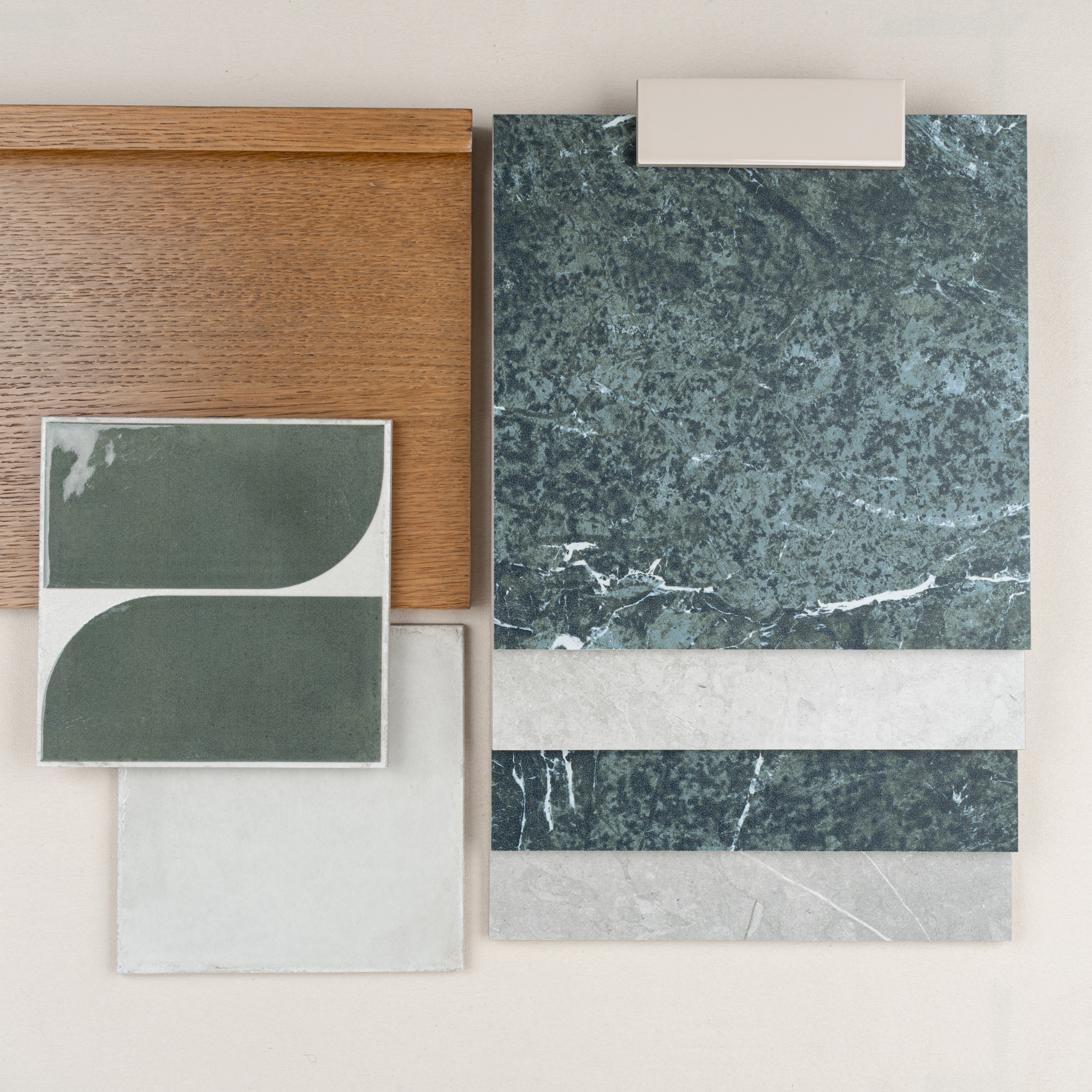 Flat lay of green marble and stone tile samples with green patterned ceramic tile and warm oak wood panel on beige background