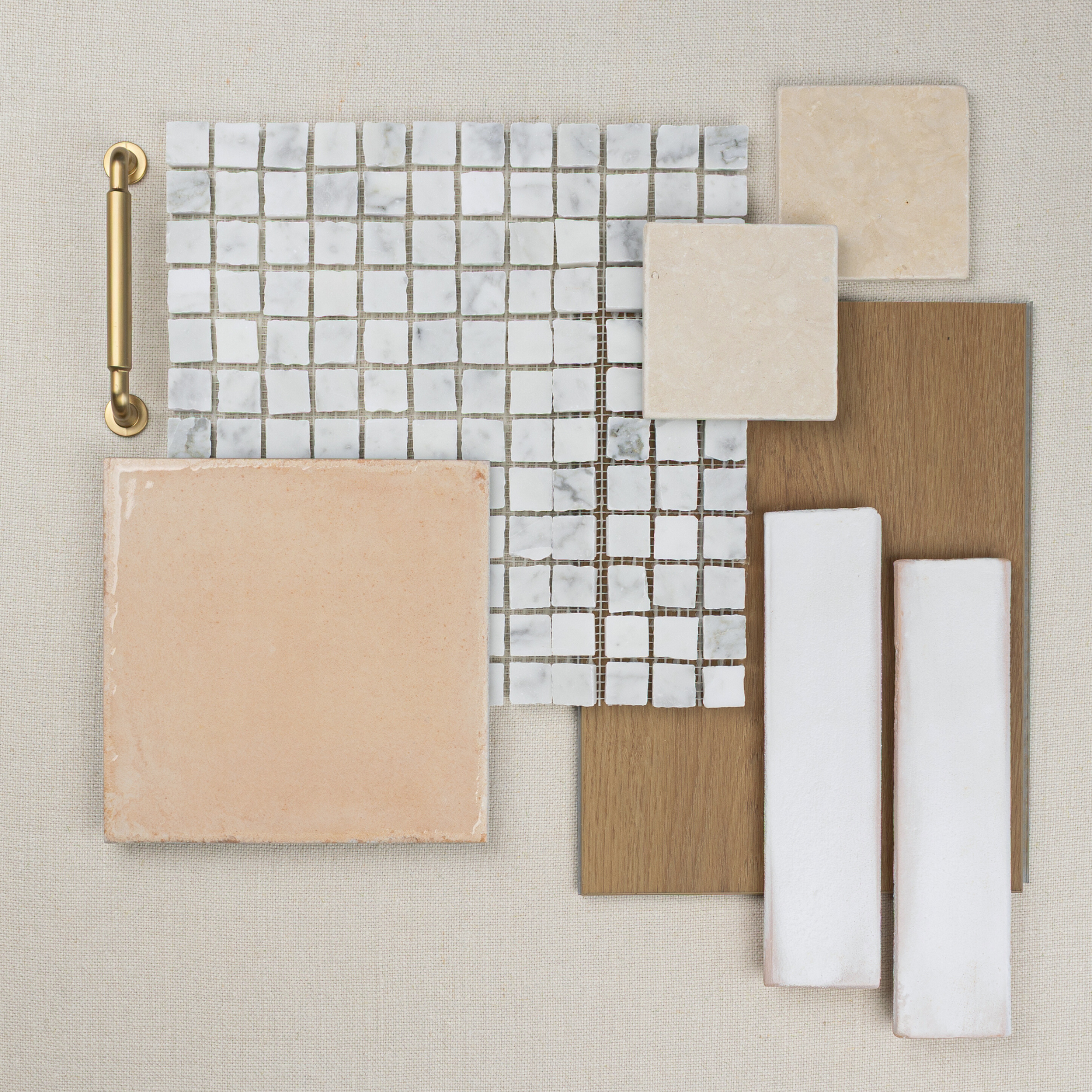Flat lay of beige ceramic tile, white marble mosaic, oak wood planks, and brass handle on neutral fabric background