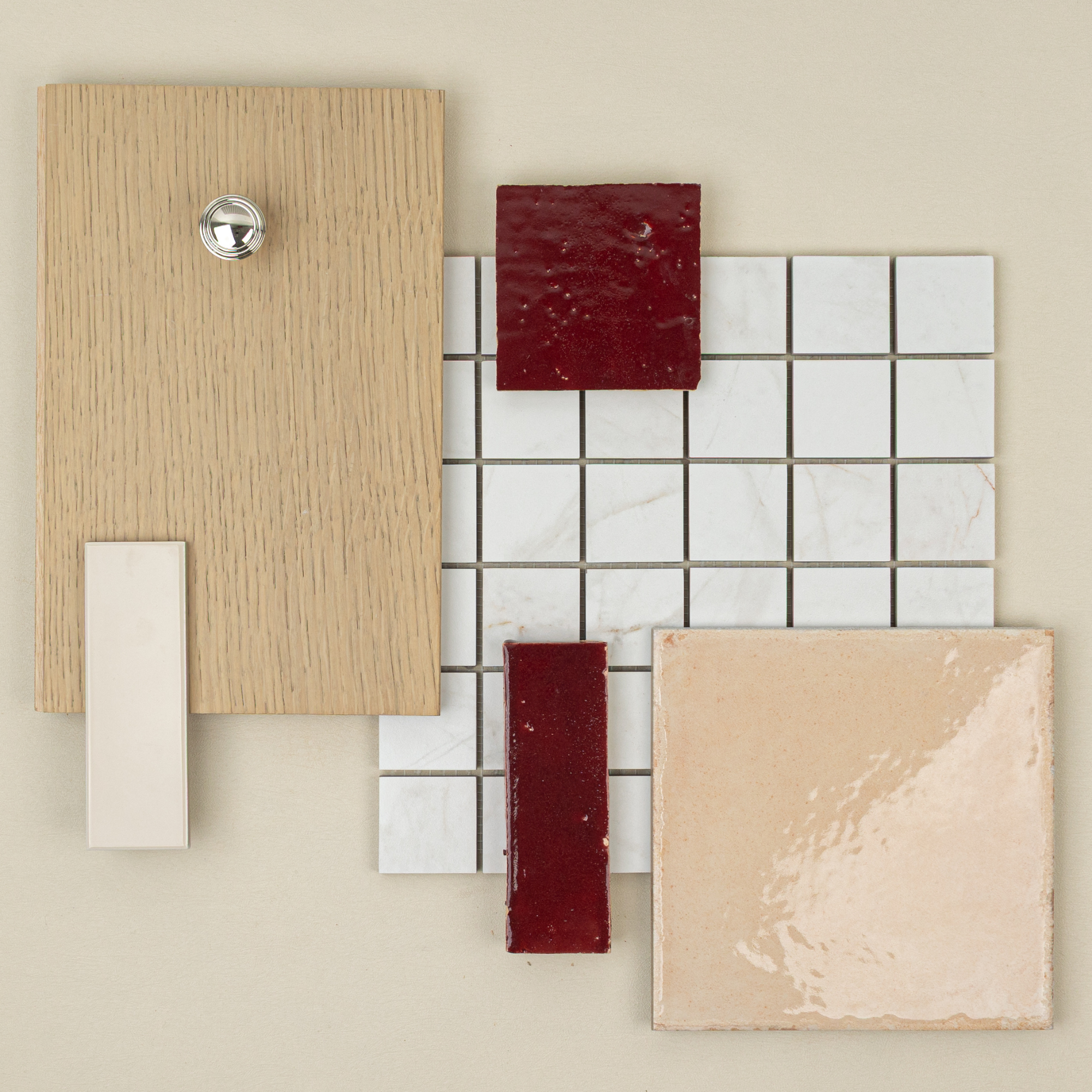 Flat lay of oak wood plank, white marble mosaic tile, glossy beige tile, and deep red ceramic tile samples on beige surface