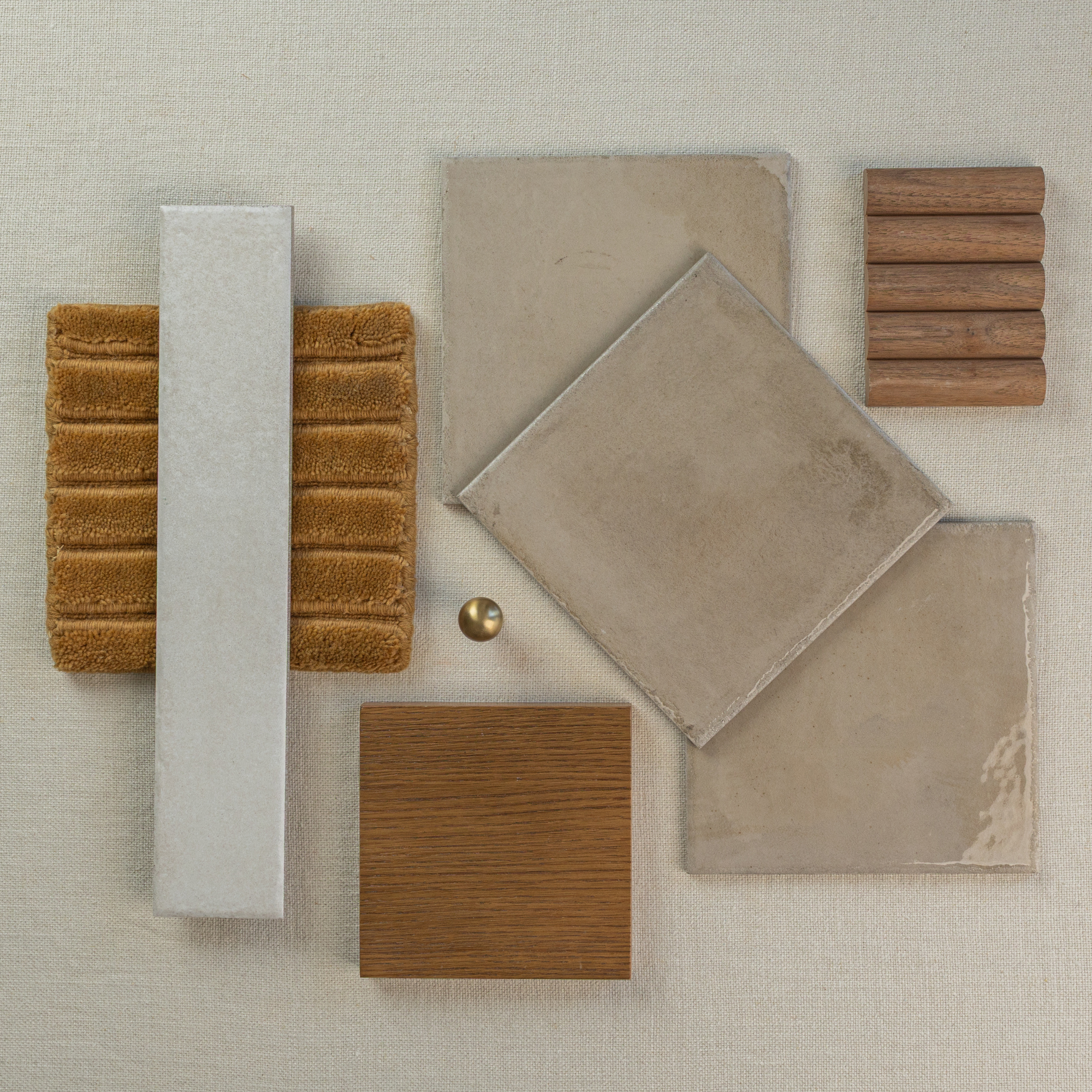 Arrangement of beige ceramic tiles, brown wood samples, textured fabric swatch, and brass hardware on neutral linen background