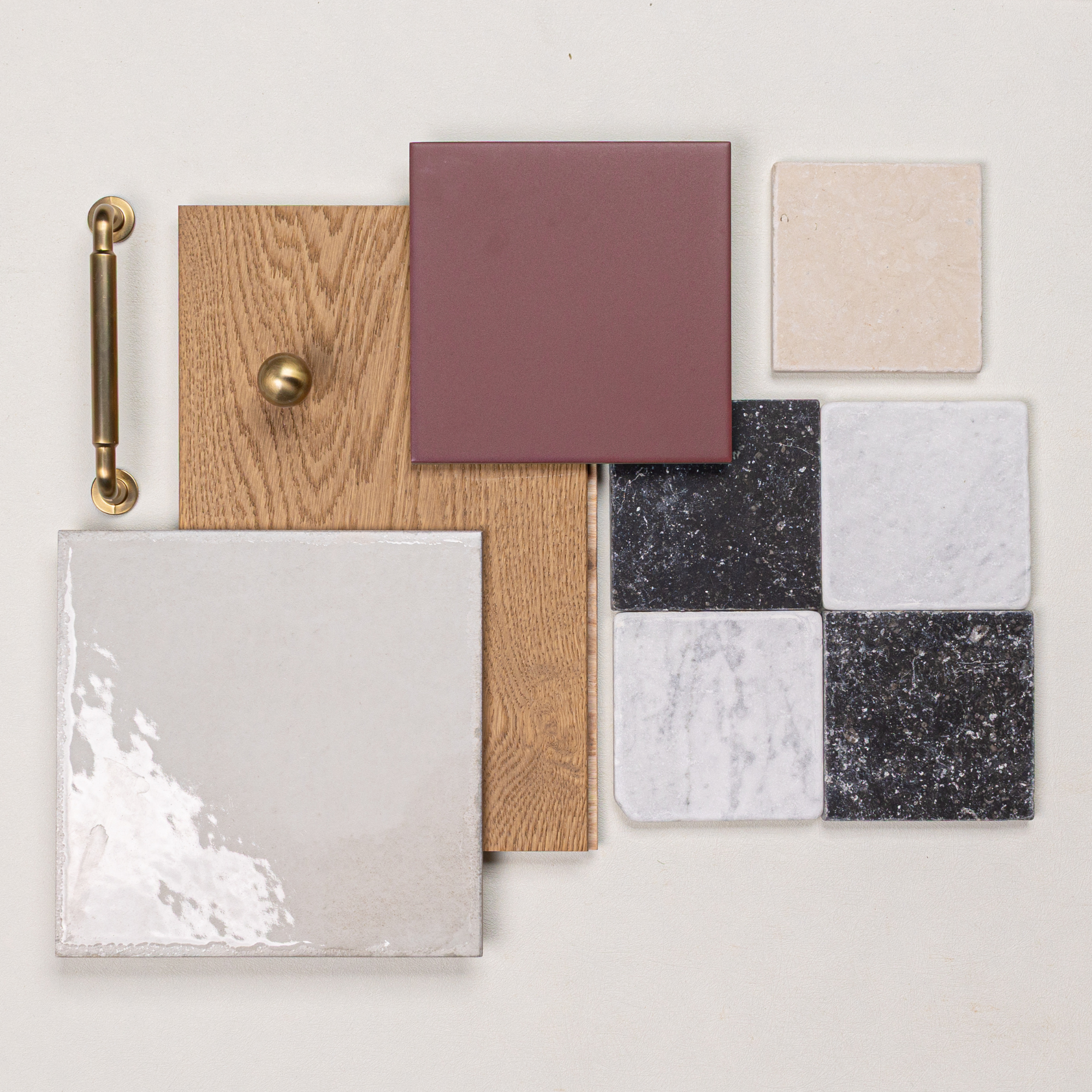 Glossy cream ceramic tile, oak wood sample with brass knob and handle, matte terracotta tile, and textured black and white marble tiles arranged on white surface