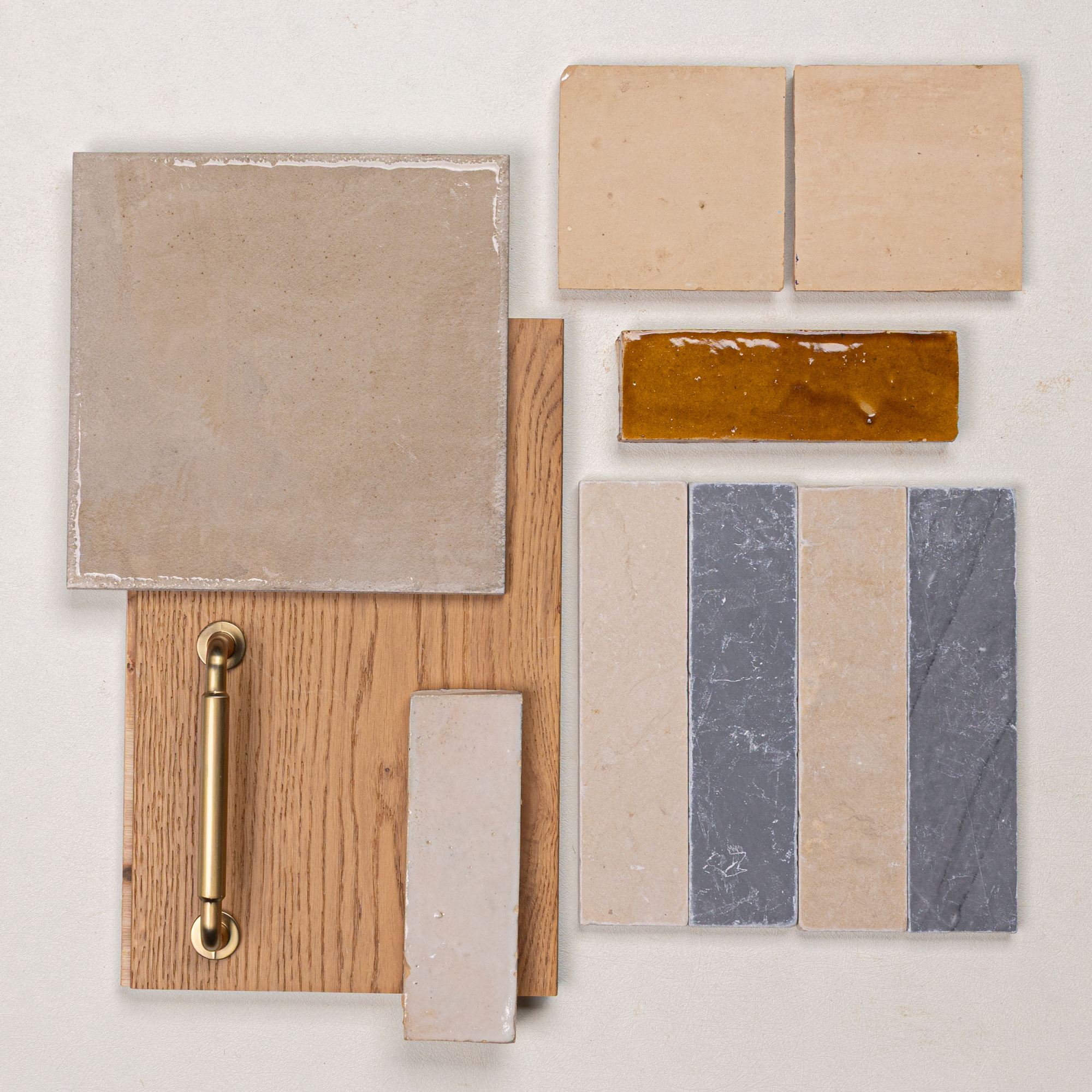 Assorted ceramic and porcelain tiles with natural oak wood and a brass handle arranged on a neutral background