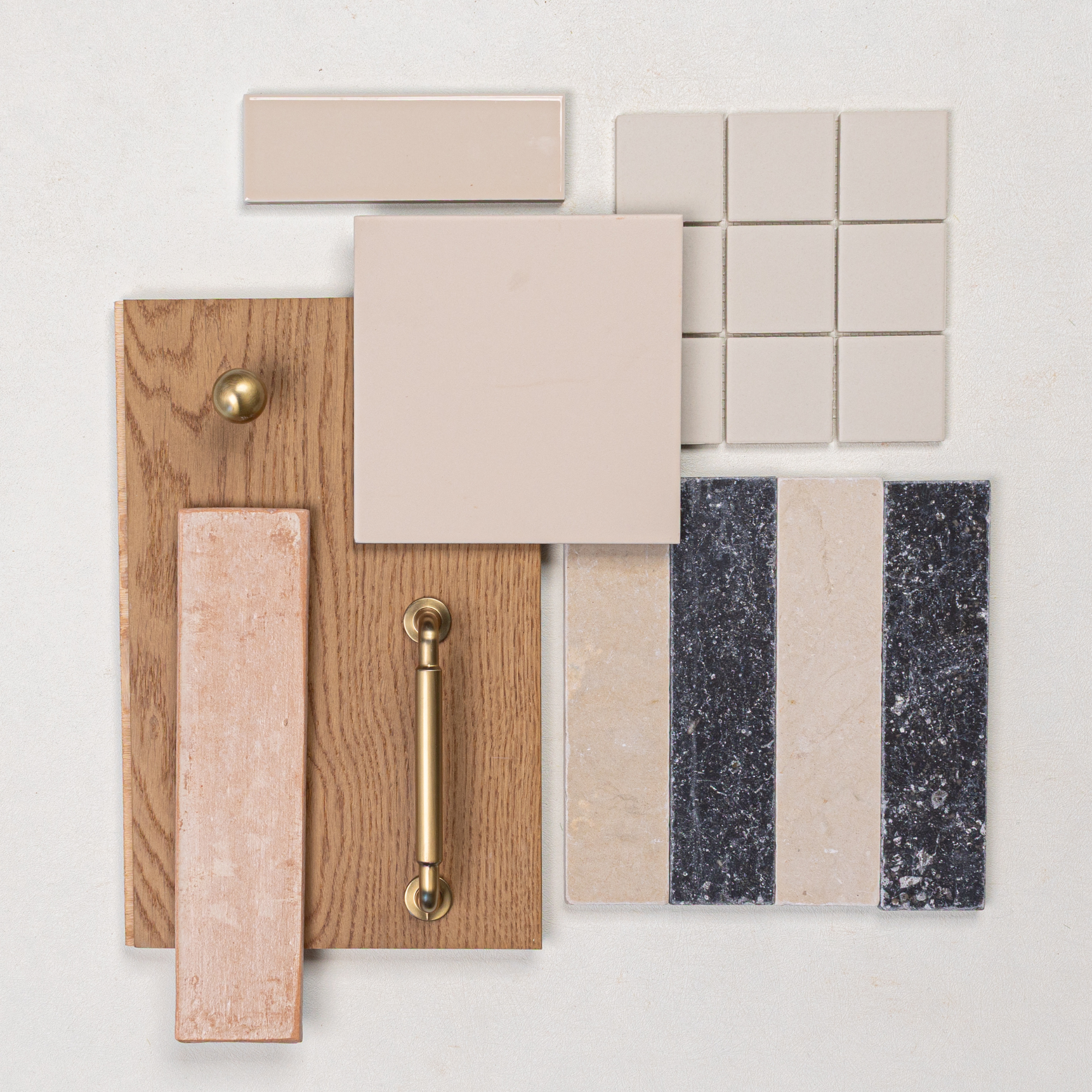 Flat lay of oak wood samples, brass hardware, beige ceramic tiles, light pink glazed tile, and black and beige striped stone tiles