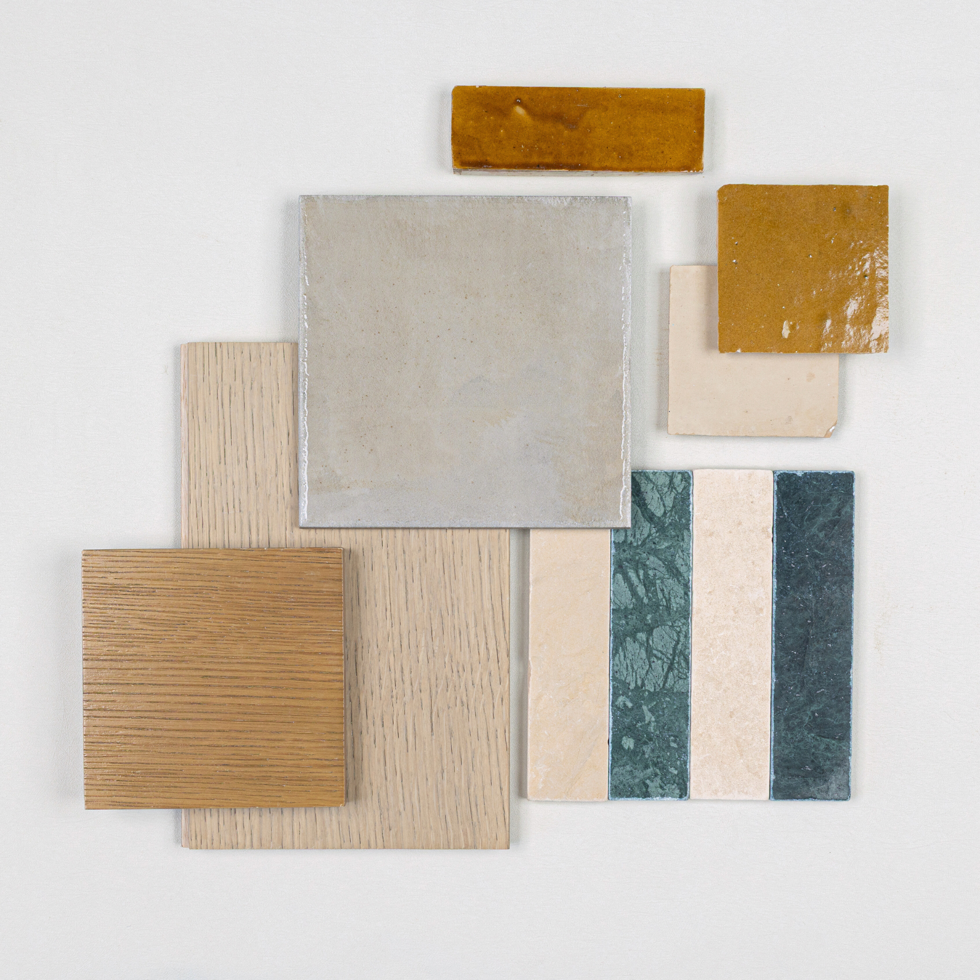 Flat lay of beige and green ceramic tiles, mustard yellow glazed tiles, and light oak wood samples on white surface