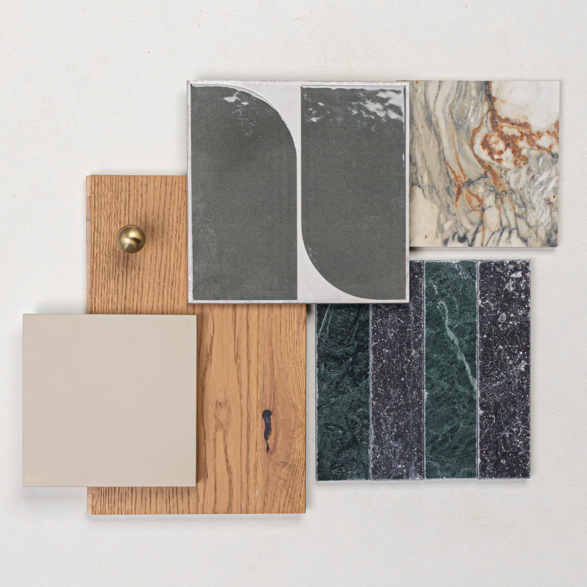 Arrangement of green marble, beige ceramic tile, curved two-tone tile, marble, oak wood, and brass knob on a pale background
