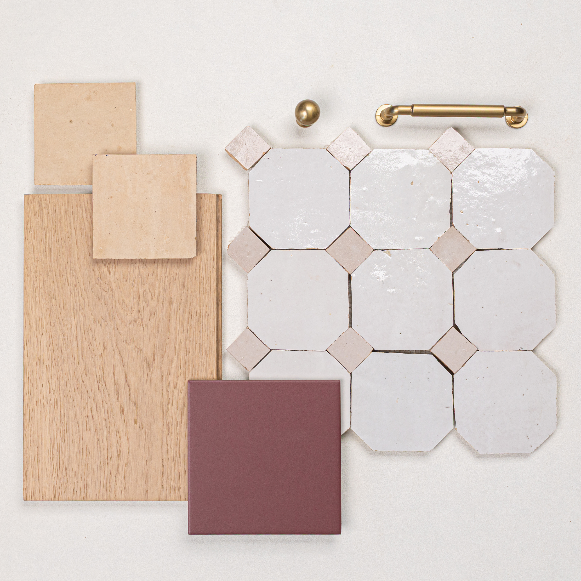Flat lay of white octagonal ceramic tiles with beige accents, oak wood sample, beige tiles, burgundy tile, and brass hardware pieces