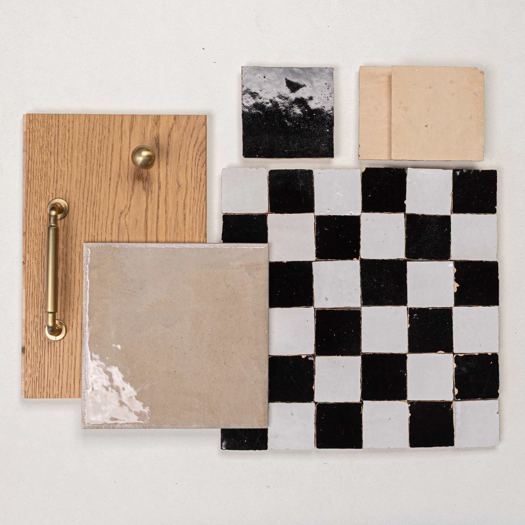 Flat lay of oak wood panel with brass handle and knob, black and white checkerboard tiles, and beige ceramic tile samples on white background