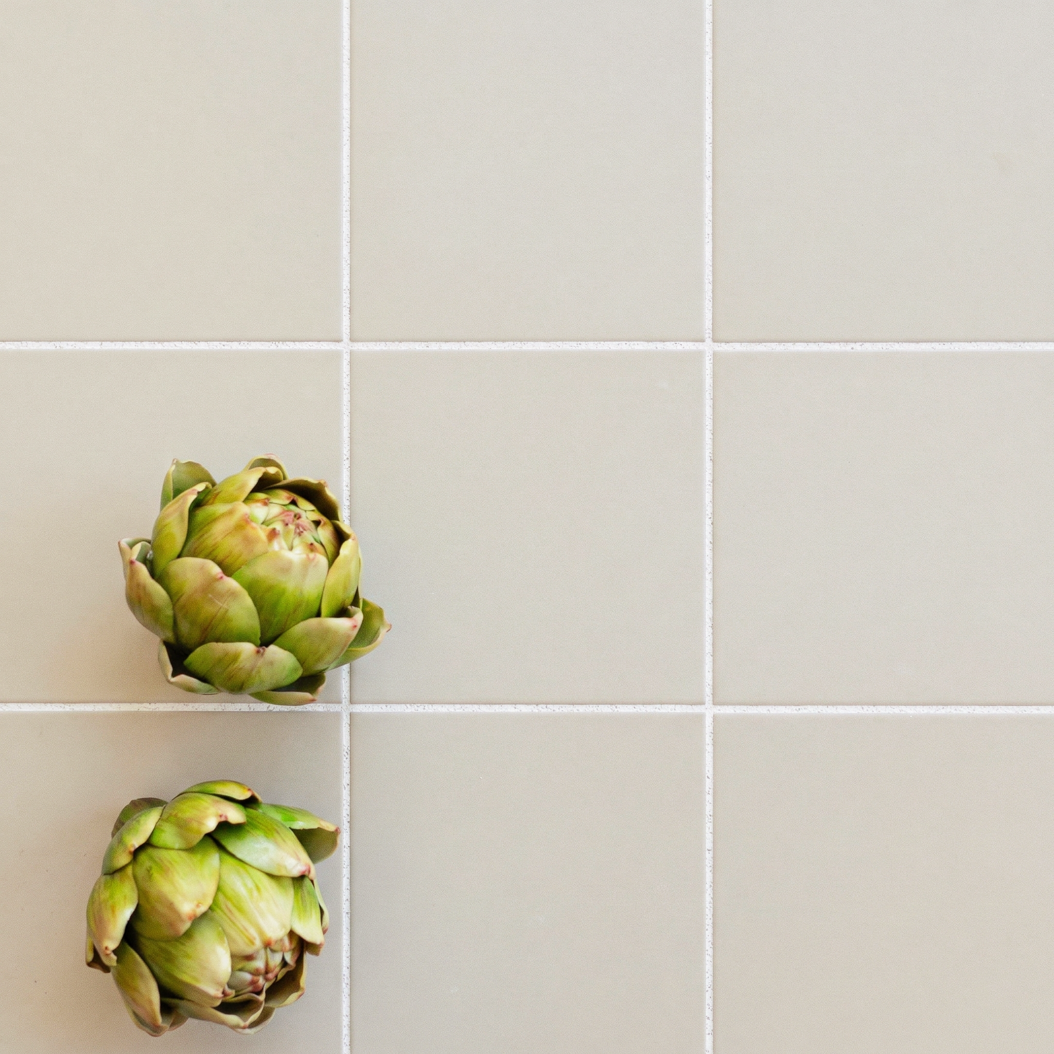 Matte porcelain tiles in soft sand color arranged in a grid with two fresh green artichokes on top