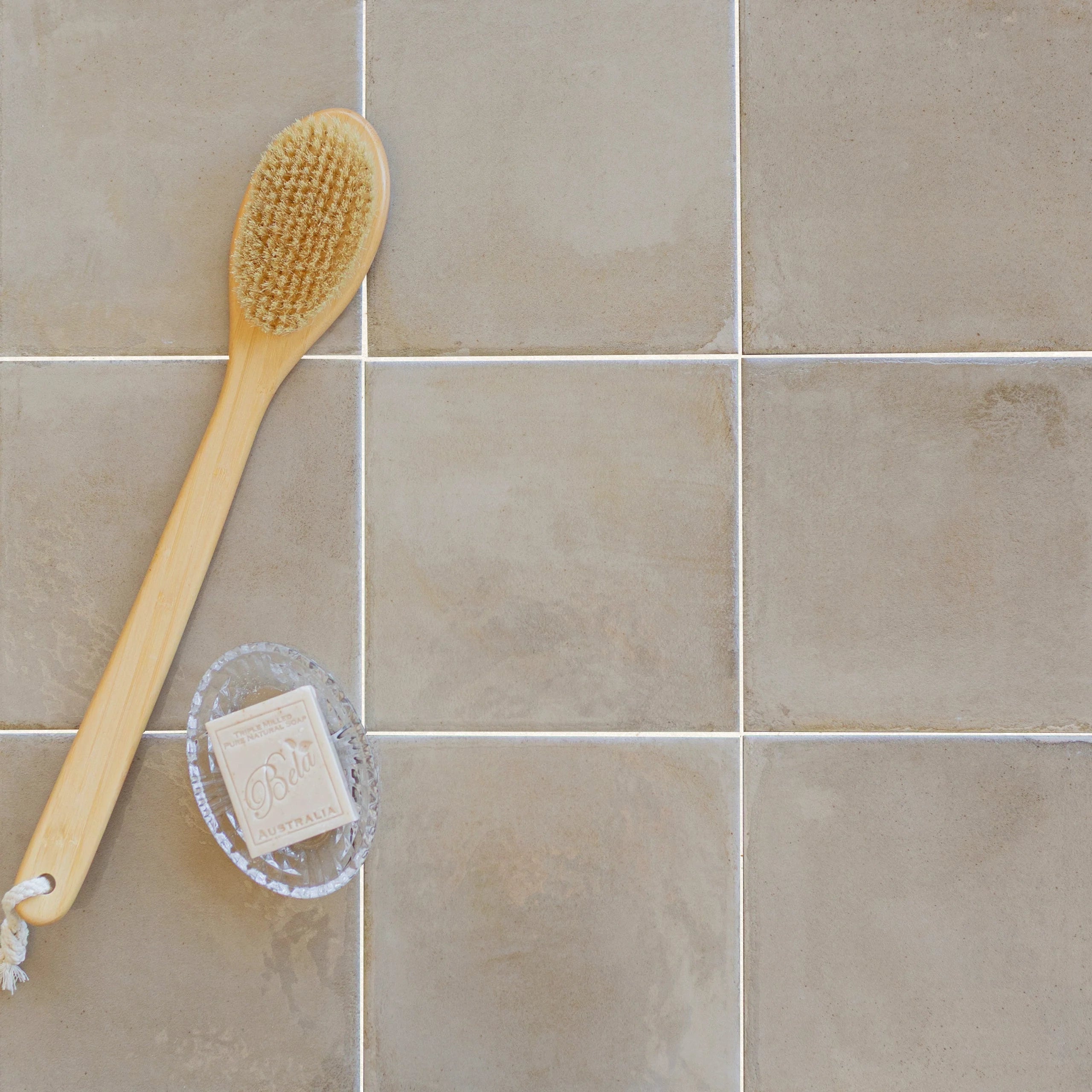 Glossy sand-colored porcelain tiles paired with a natural wooden bath brush and a rectangular soap bar on a tiled surface