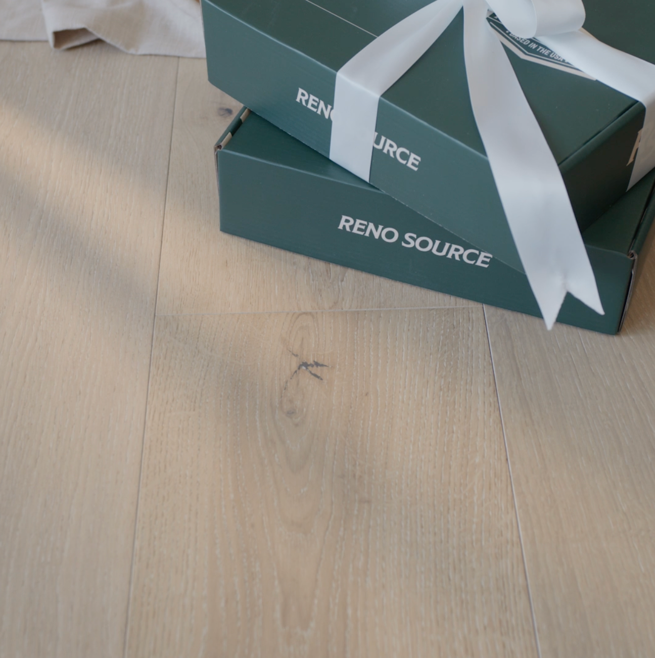 Light natural oak engineered wood flooring with two green gift boxes tied with white ribbon resting on top