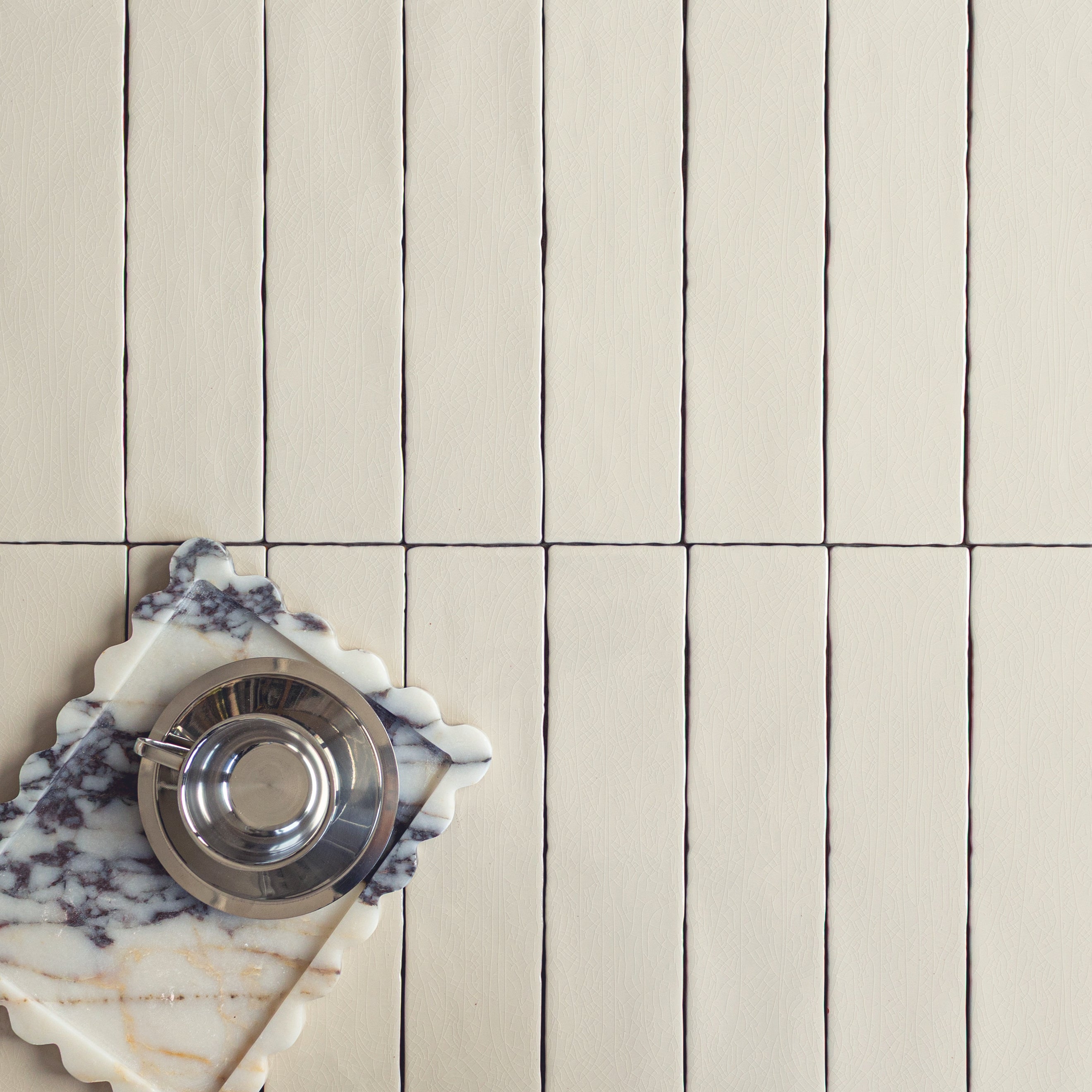 Matte cream ceramic tiles arranged vertically with subtle grout lines alongside a marble board and a silver cup on top