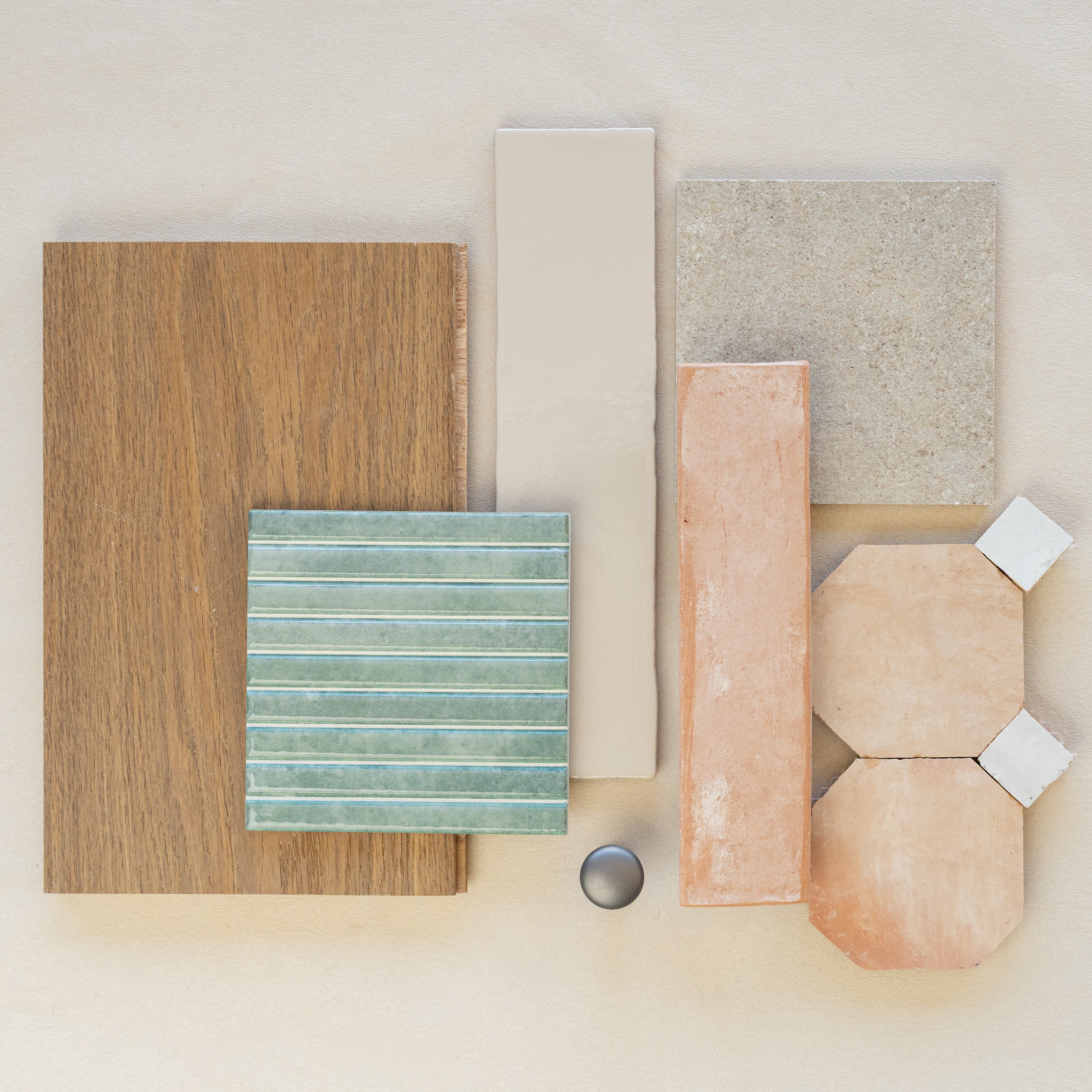 Flat lay of oak wood plank, green ceramic tile, soft beige and terracotta tiles, gray stone square, and round metal knob on neutral surface