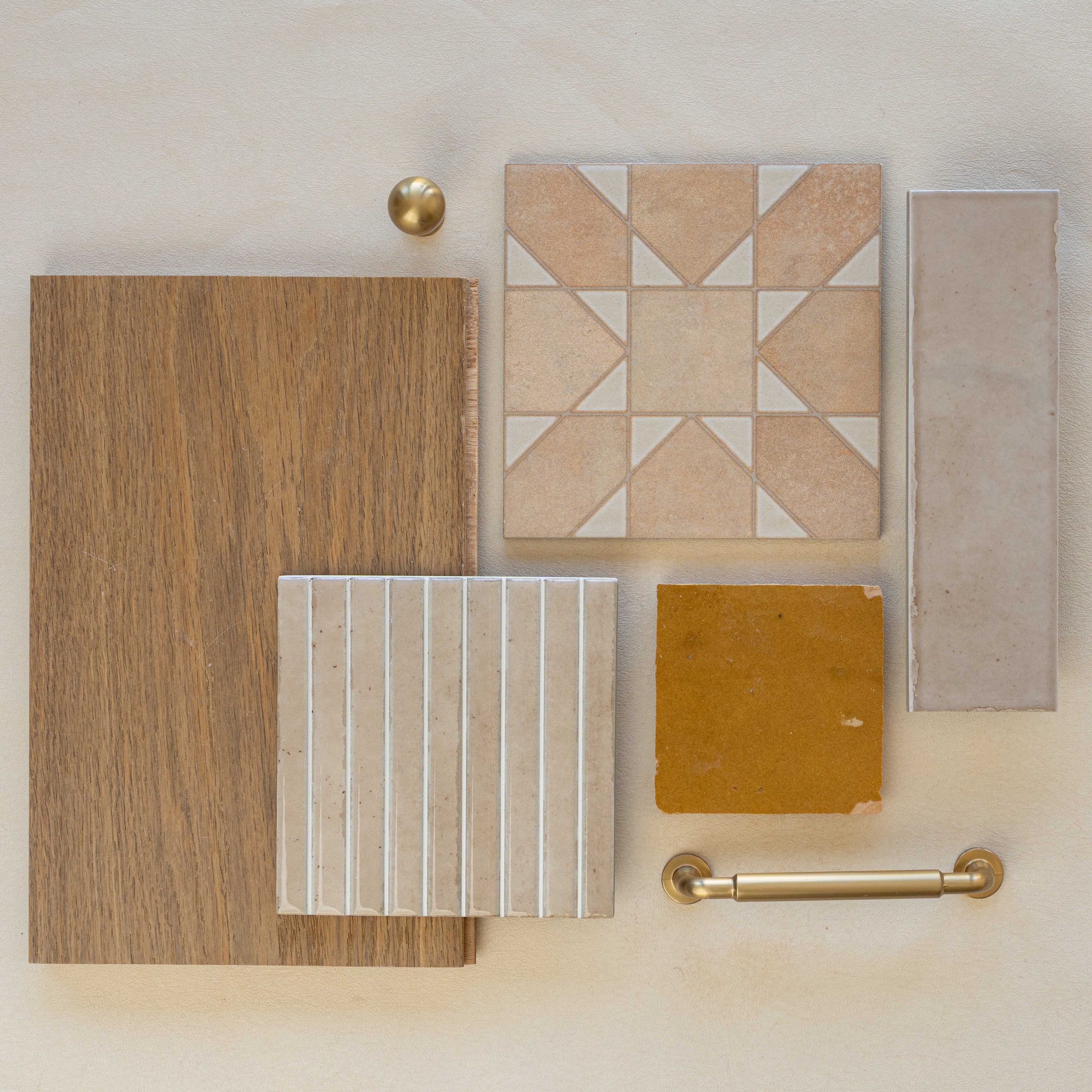 Flat lay of oak wood sample, beige patterned ceramic tile, mustard porcelain tile, taupe rectangular tile, and brass hardware on neutral background