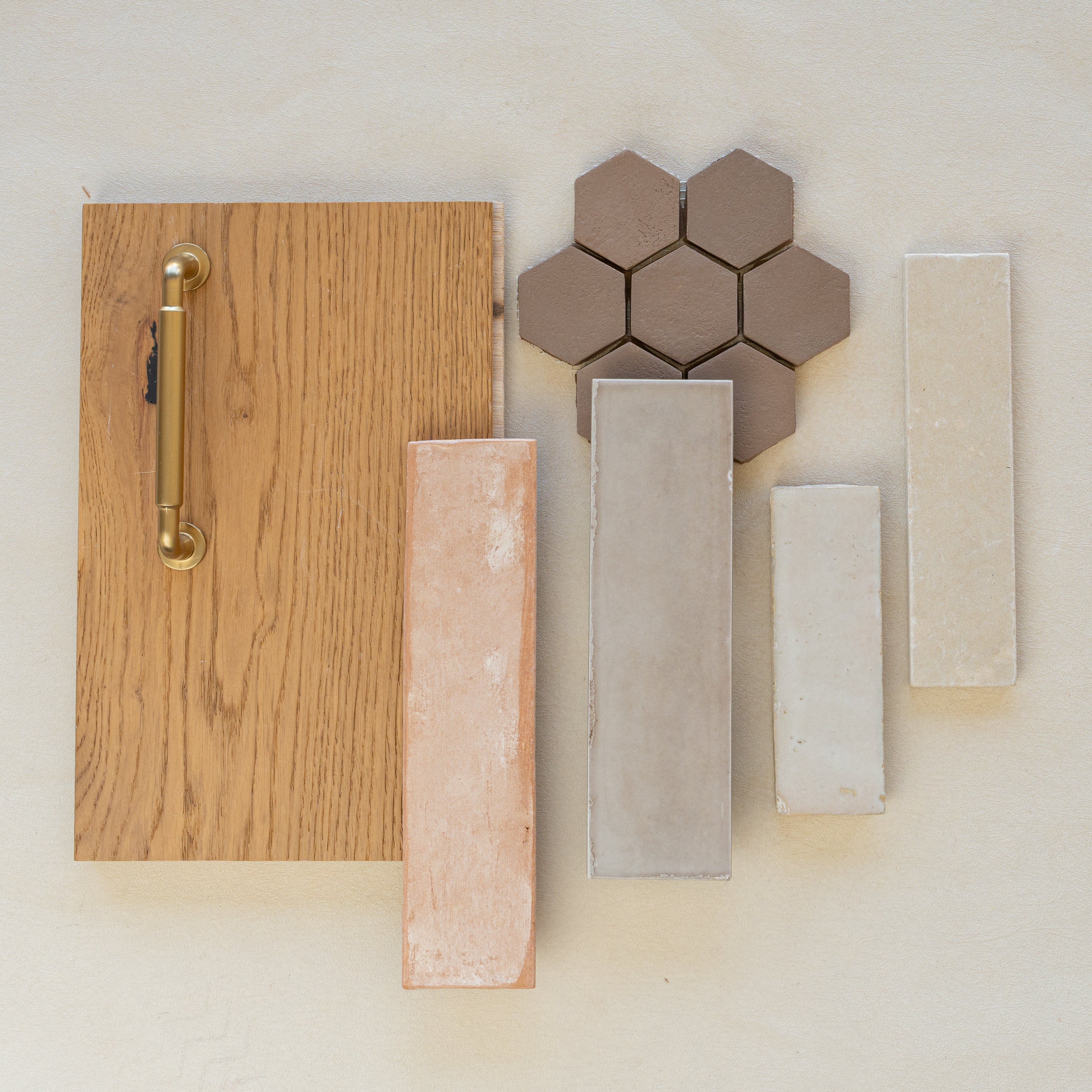 Arrangement of oak wood sample with brass handle, hexagonal brown ceramic tiles, and rectangular beige and gray porcelain tiles on neutral surface