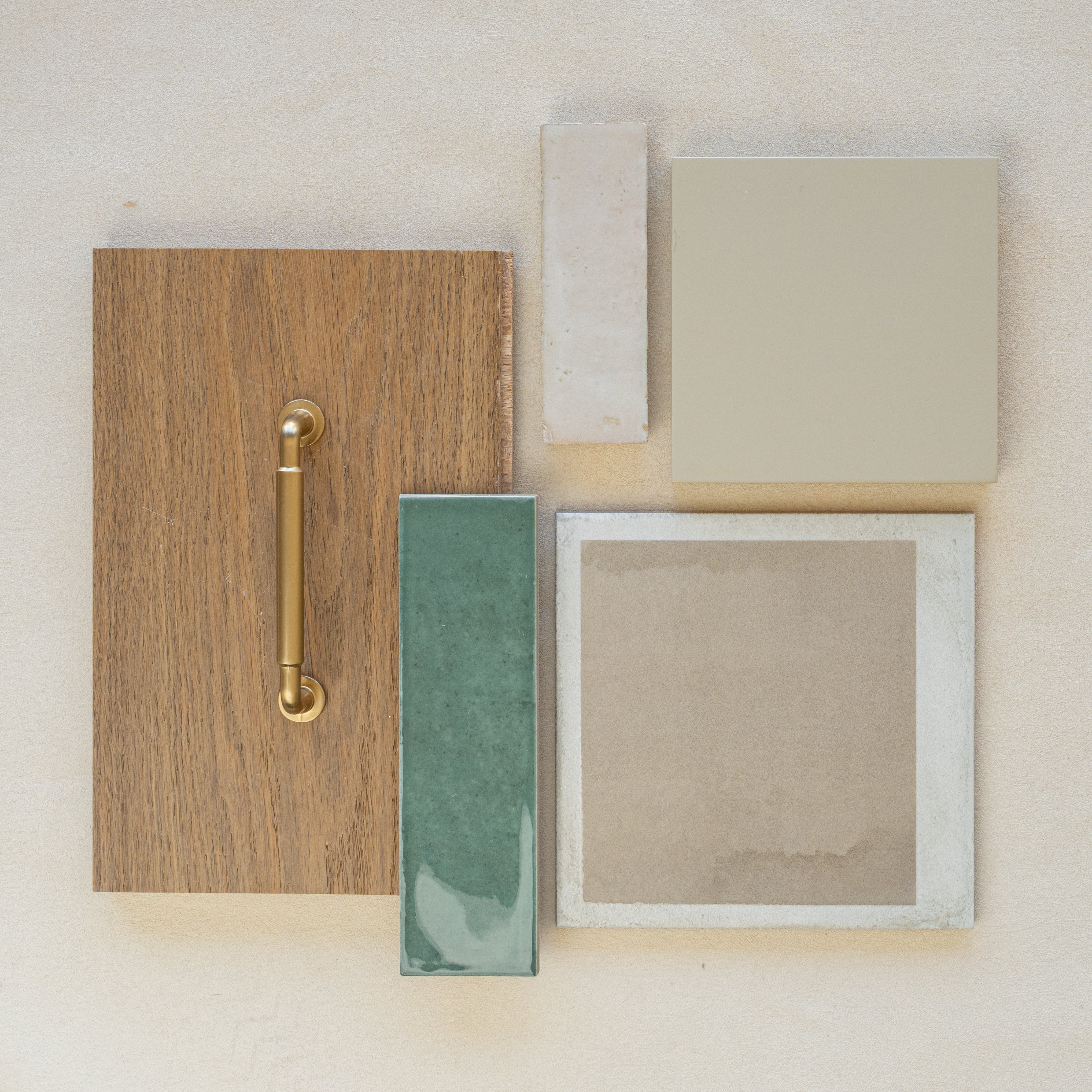 Flat lay of oak wood sample with brass handle, green ceramic tile, beige ceramic square, and natural stone tile on light background