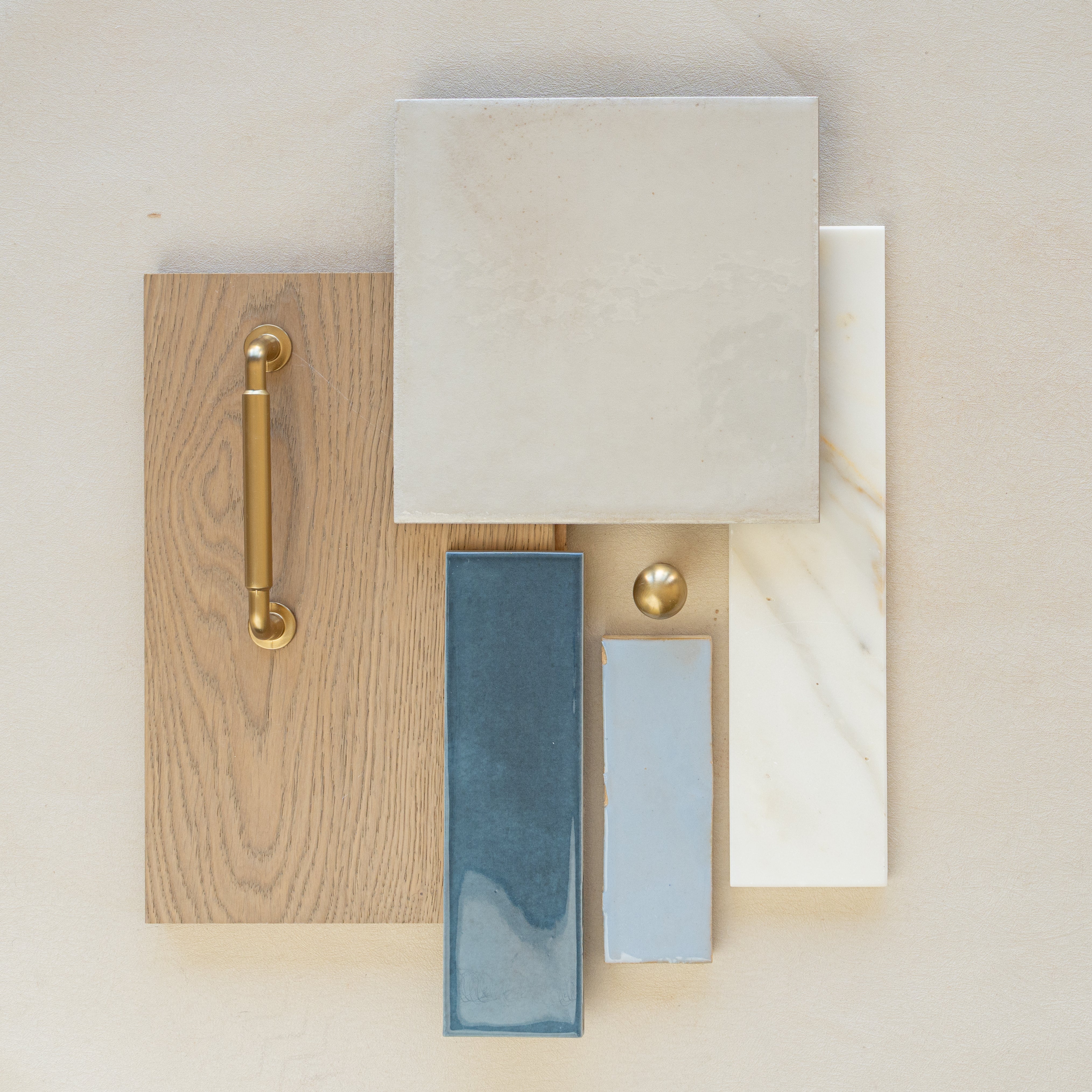 Arrangement of oak wood sample with brass handle, cream porcelain tile, blue ceramic tiles, and white marble strip on beige surface