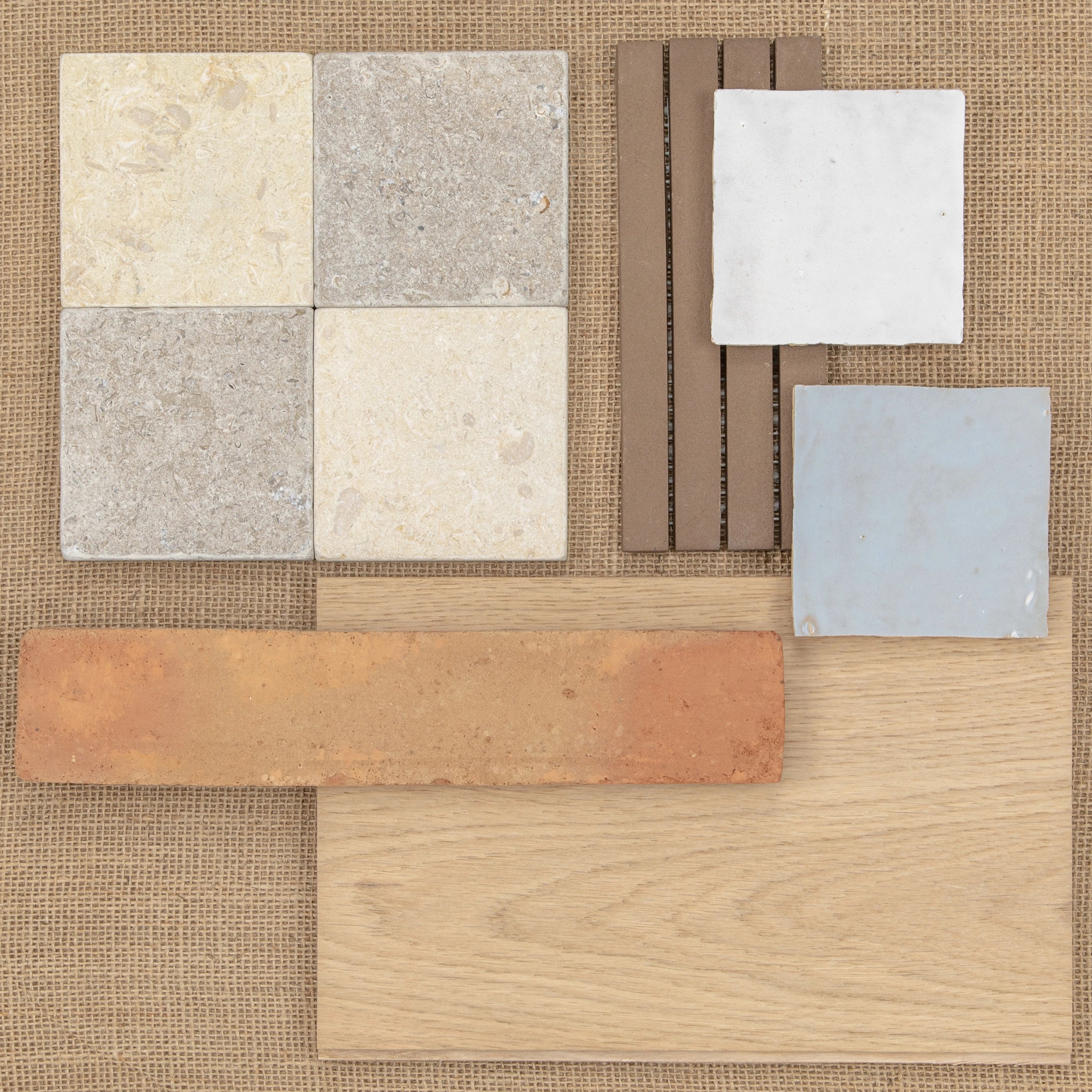 Assorted ceramic tiles, terracotta, wood, and textured samples in neutral shades on a woven fabric background.