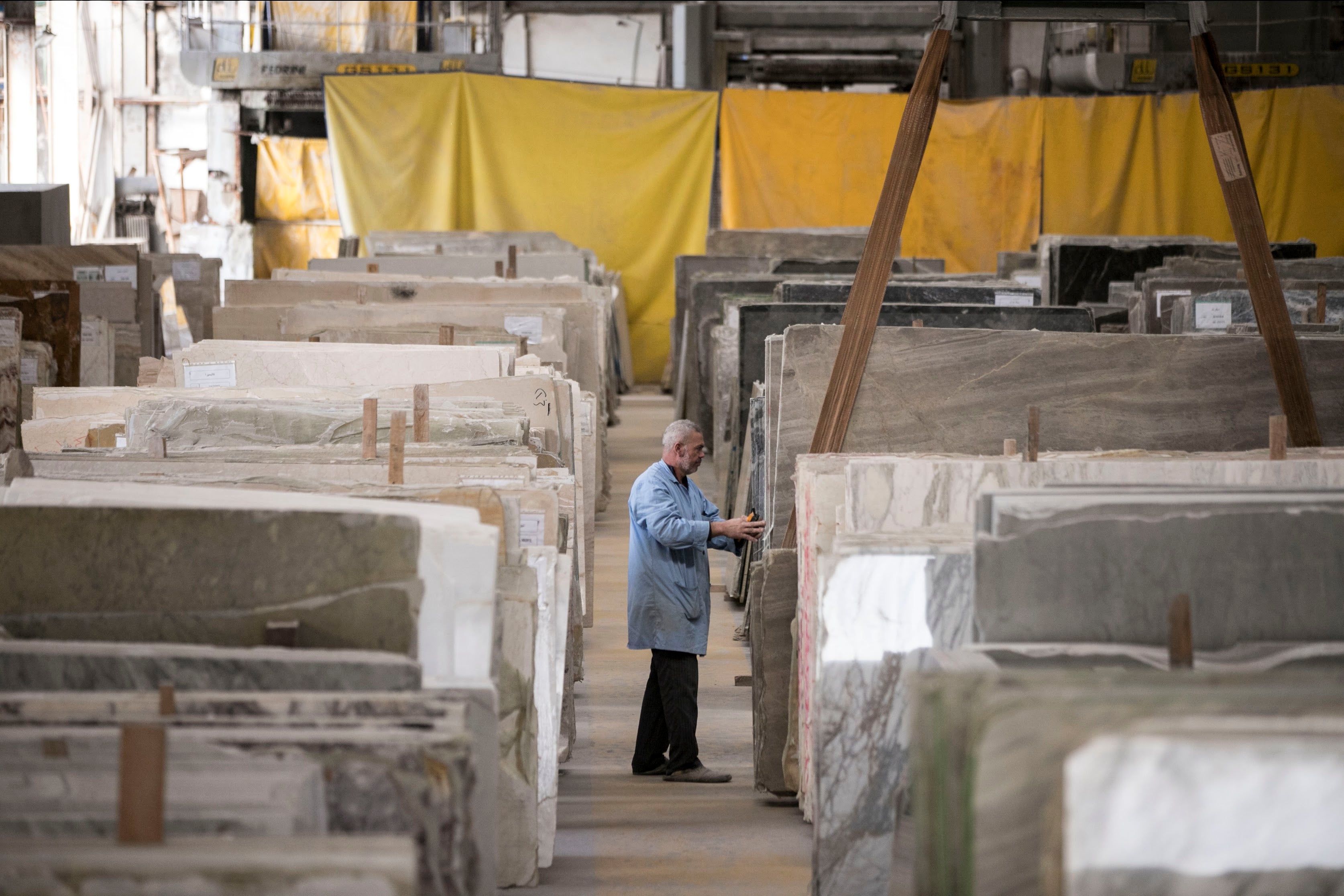 Man examining large slabs of natural stone and marble in a spacious warehouse with yellow partitions