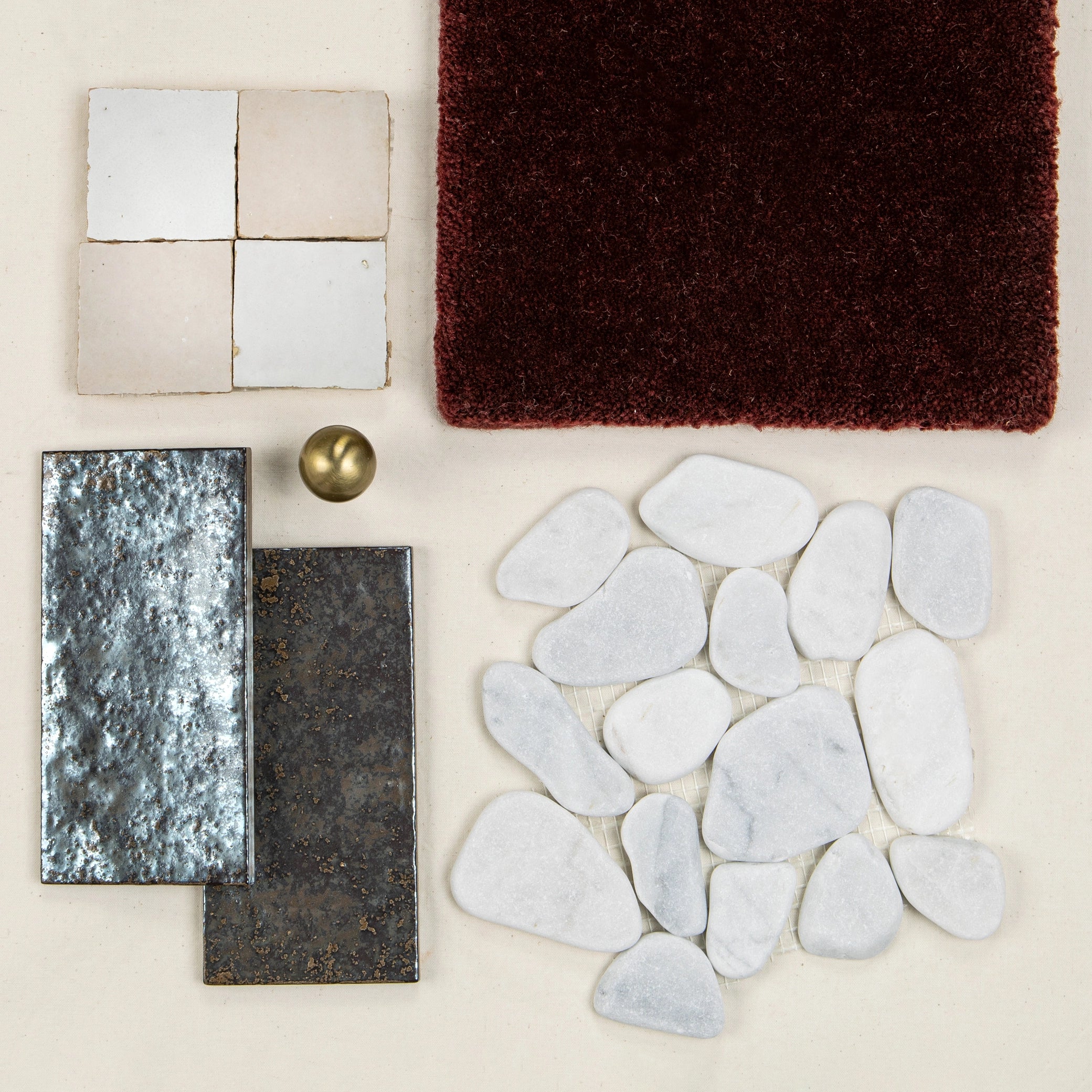 Assortment of textured porcelain and ceramic tiles with smooth white stones, brass knob, and deep red fabric swatch