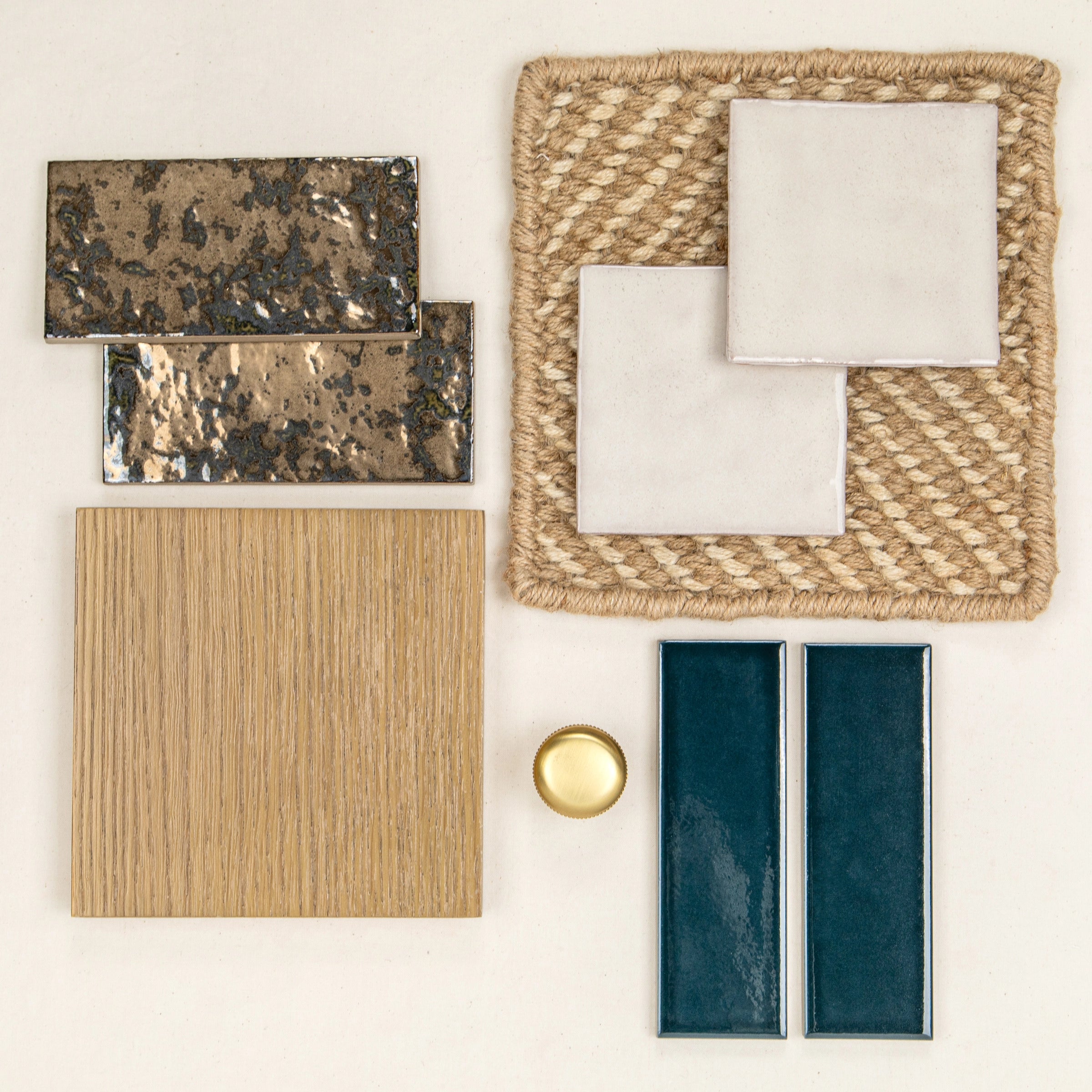 Assortment of textured ceramic tiles in bronze, creamy white, deep teal, and natural oak wood on woven mat with brass accent