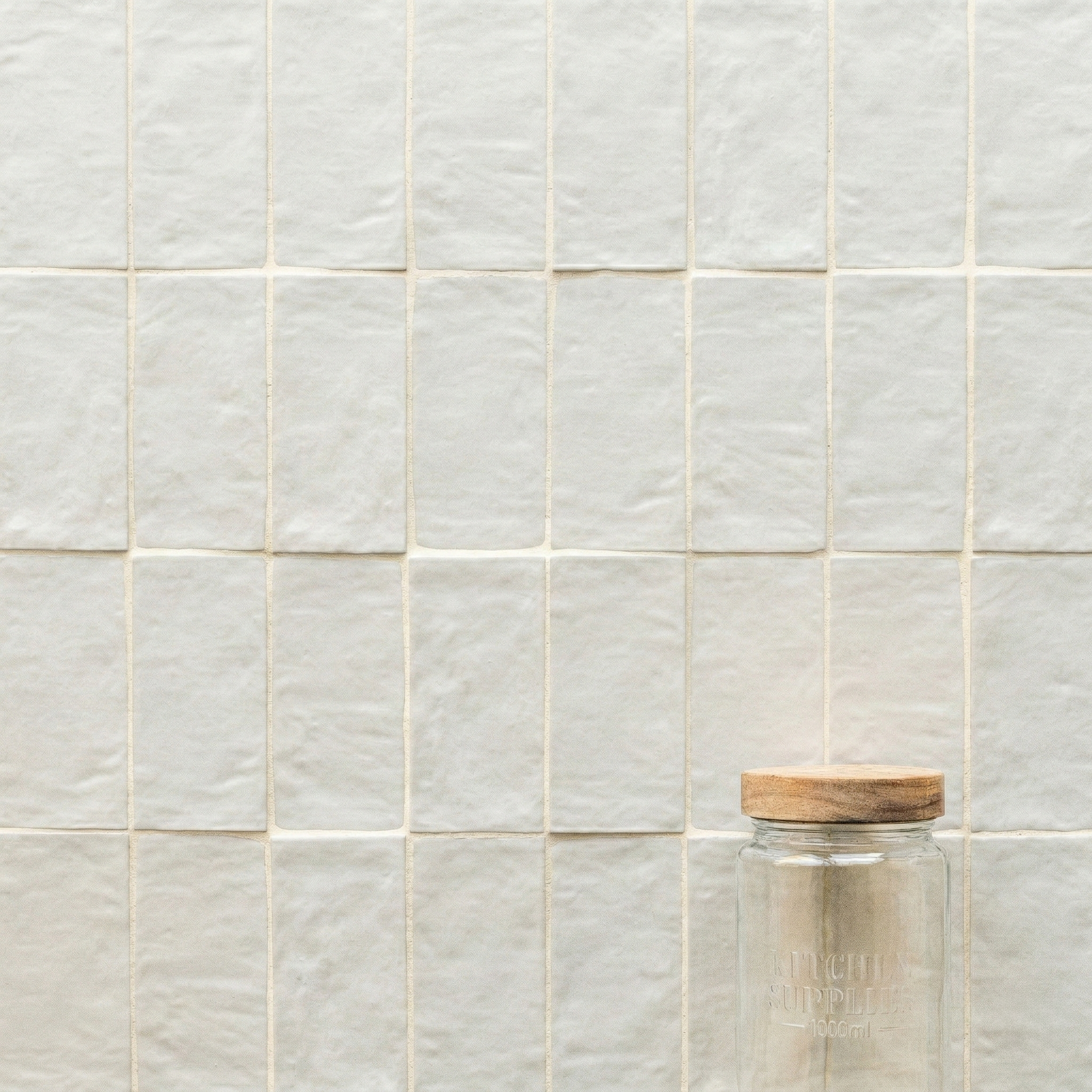 Creamy off-white textured ceramic tiles arranged in a grid with a clear glass jar topped with a wooden lid in the corner