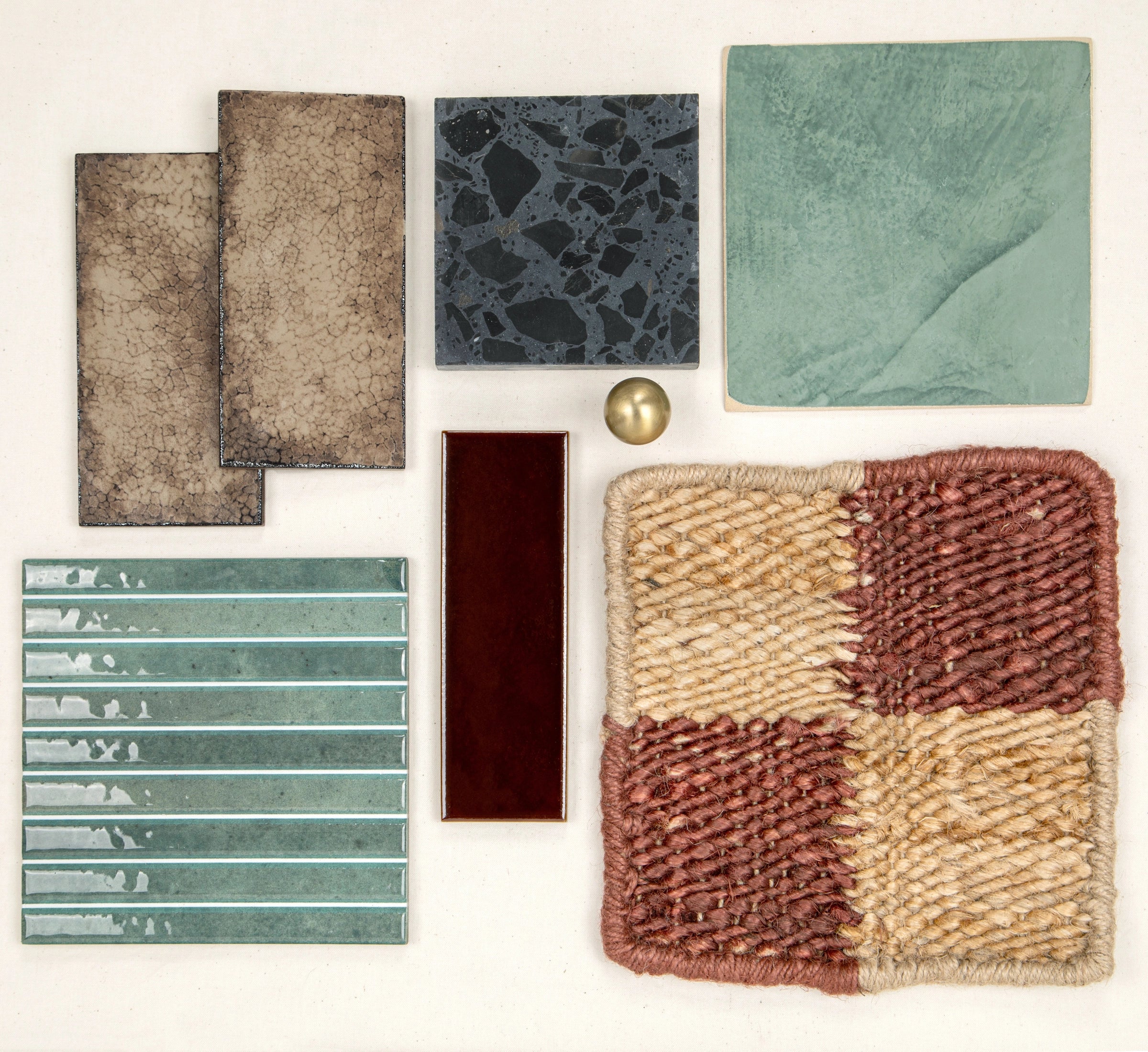 Varied ceramic and porcelain tiles in muted earth tones with a textured woven swatch and a brass accent ball