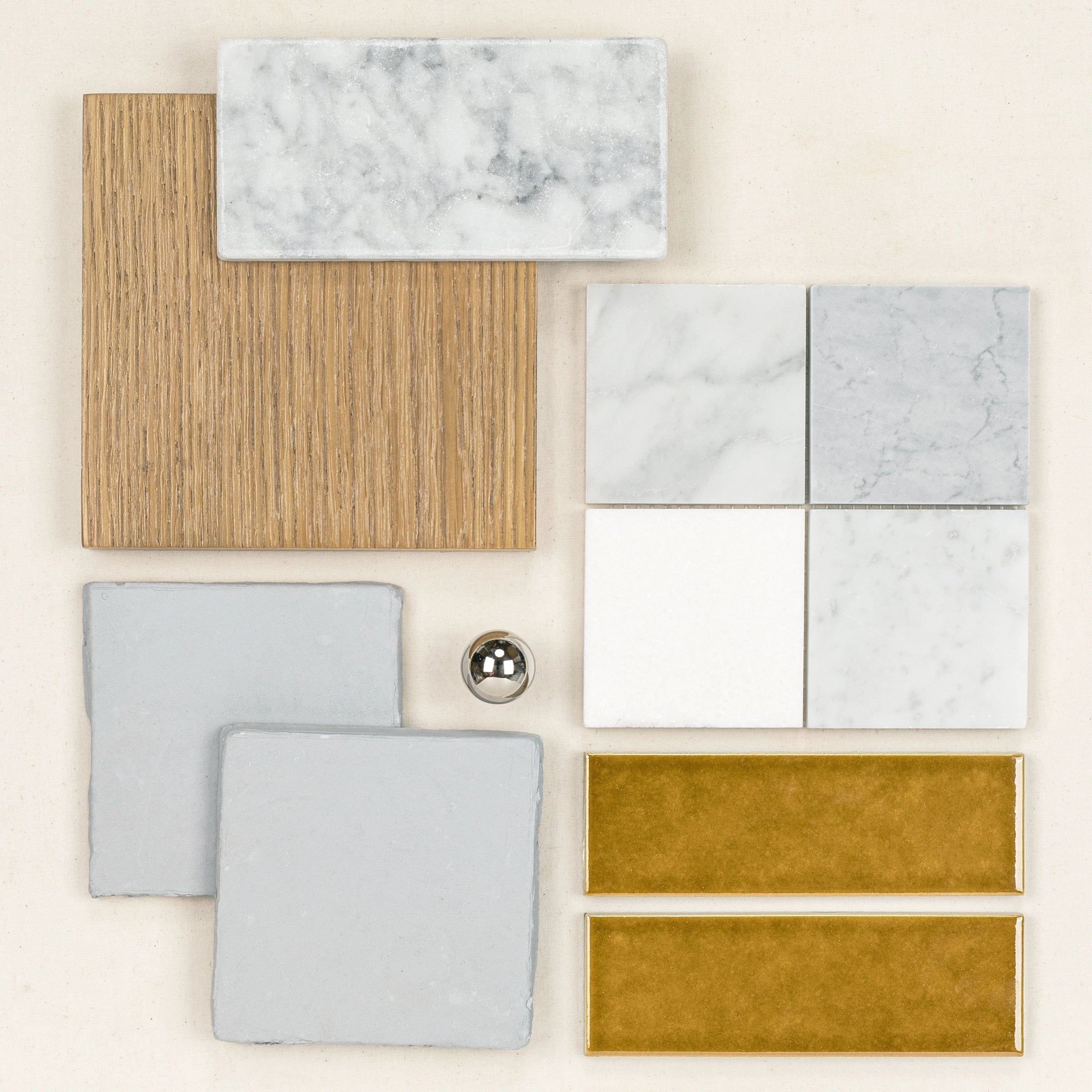 Assortment of ceramic tiles in white marble, light gray, mustard yellow, and wood textures arranged with a small reflective sphere