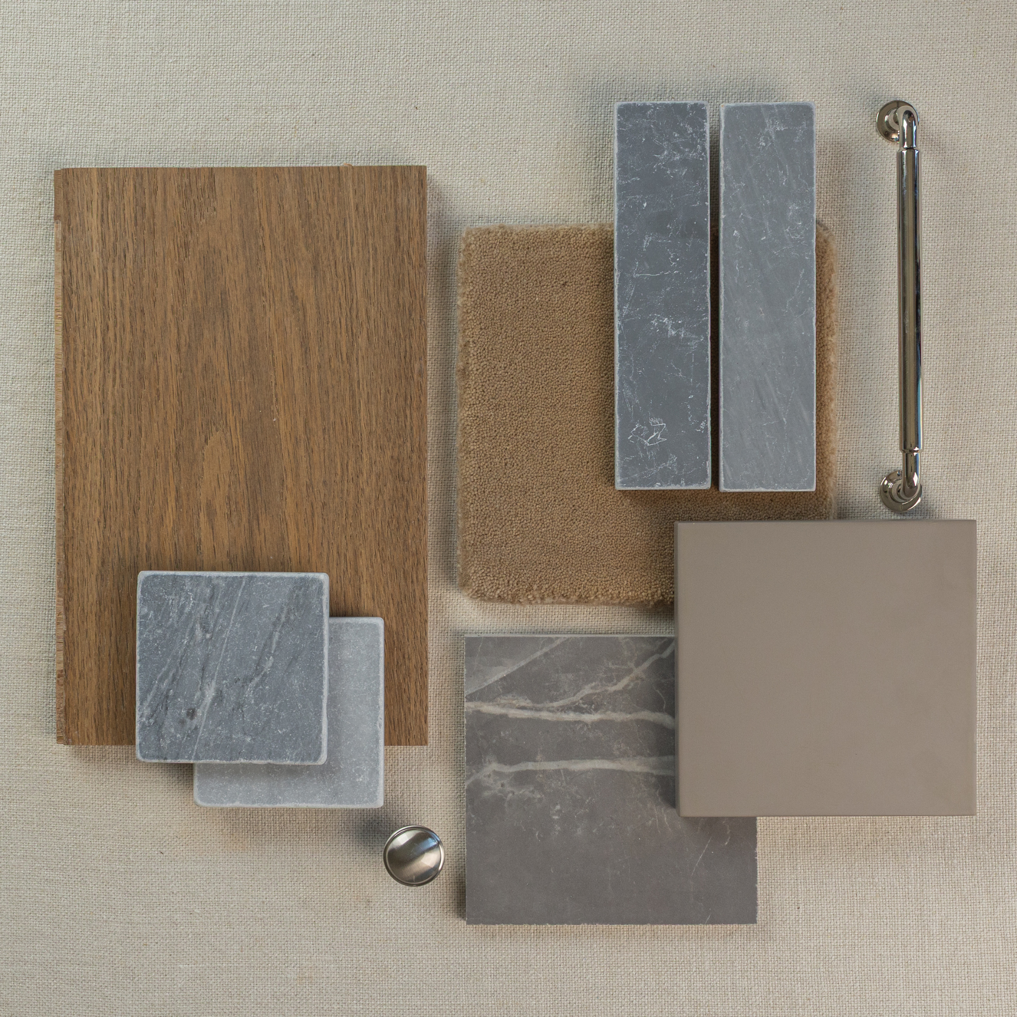 Flat lay of wood veneer, gray marble tile samples, beige ceramic tile, textured fabric swatch, and metallic hardware on neutral linen