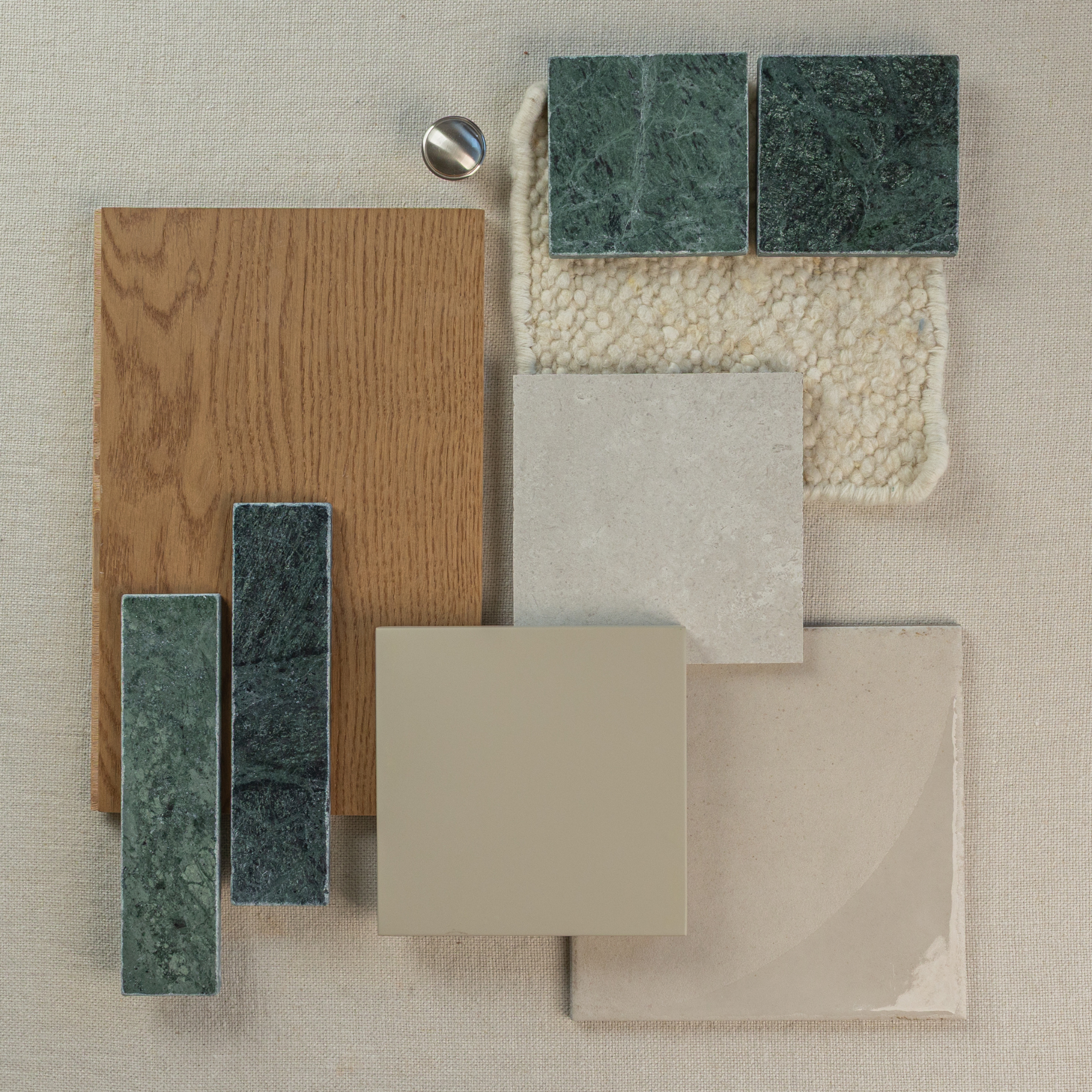 Collection of green marble tiles, beige ceramic tiles, wood veneer, and textured cream fabric on neutral background