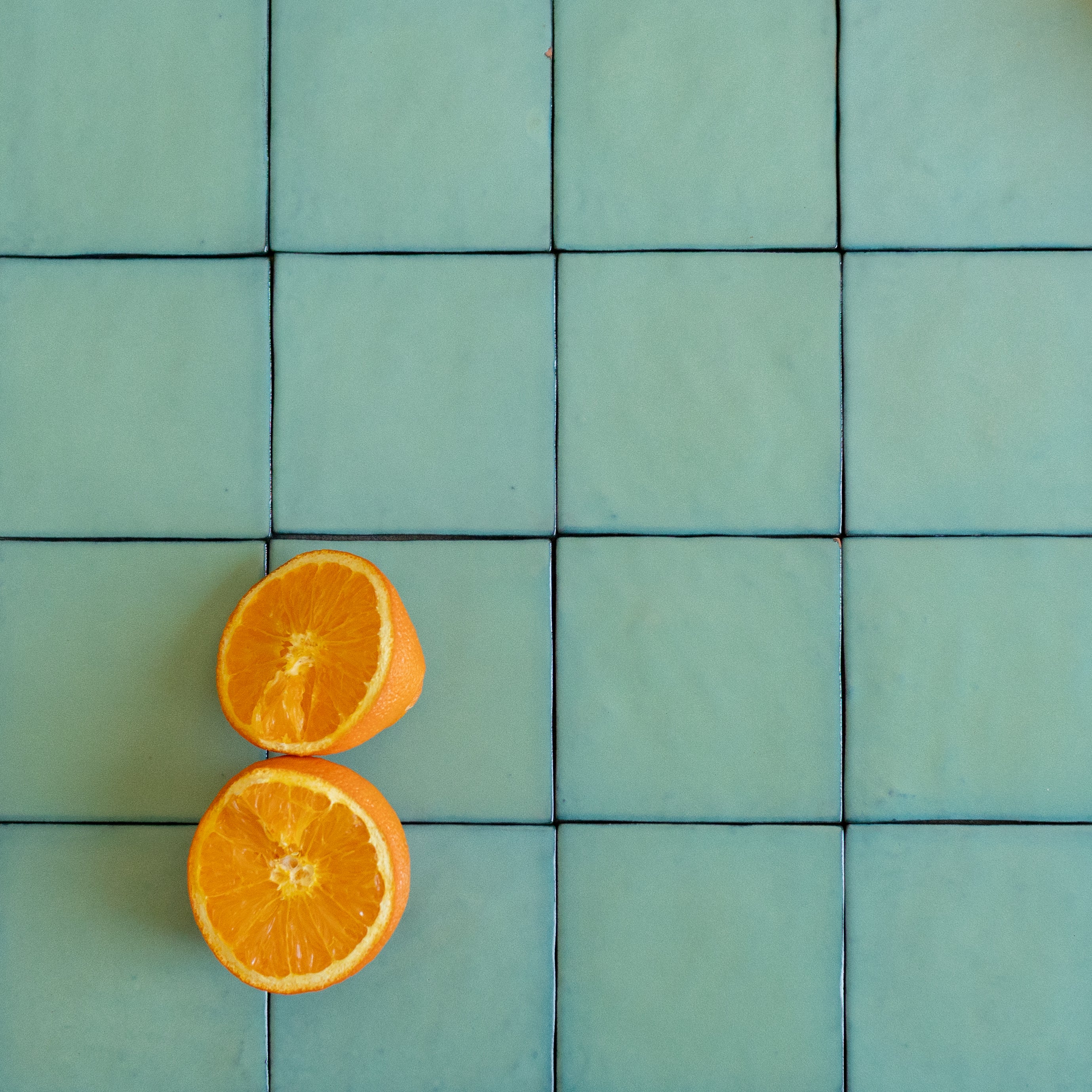 Handmade turquoise ceramic tiles with subtle texture and two orange halves placed on top for contrast