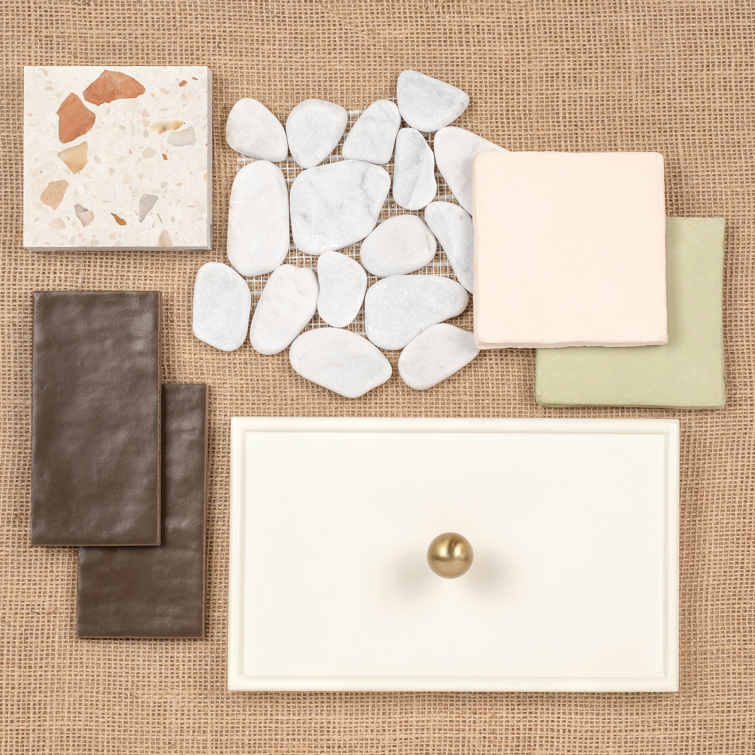 Flat lay of various tile and stone samples, including terrazzo, pebble, ceramic, and textured tiles on burlap background