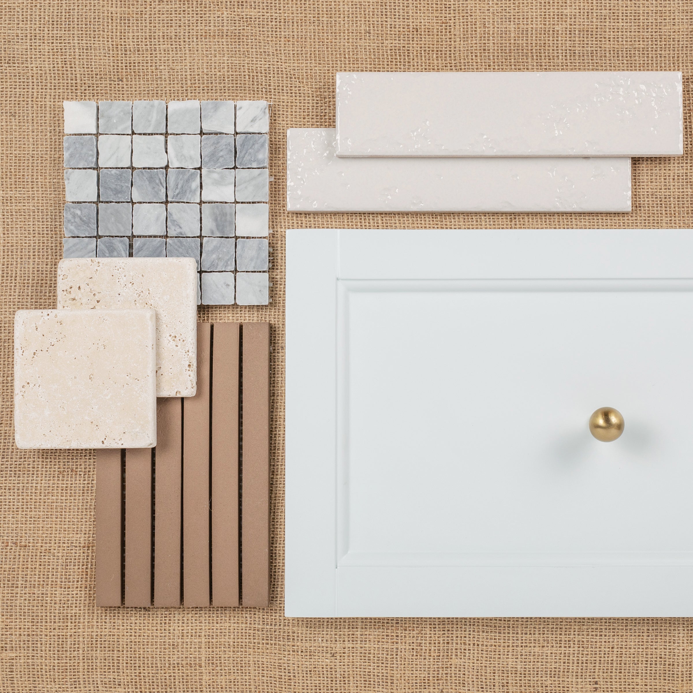 Flat lay of ceramic tiles, natural stone samples, and a white cabinet door with a round brass knob on burlap.