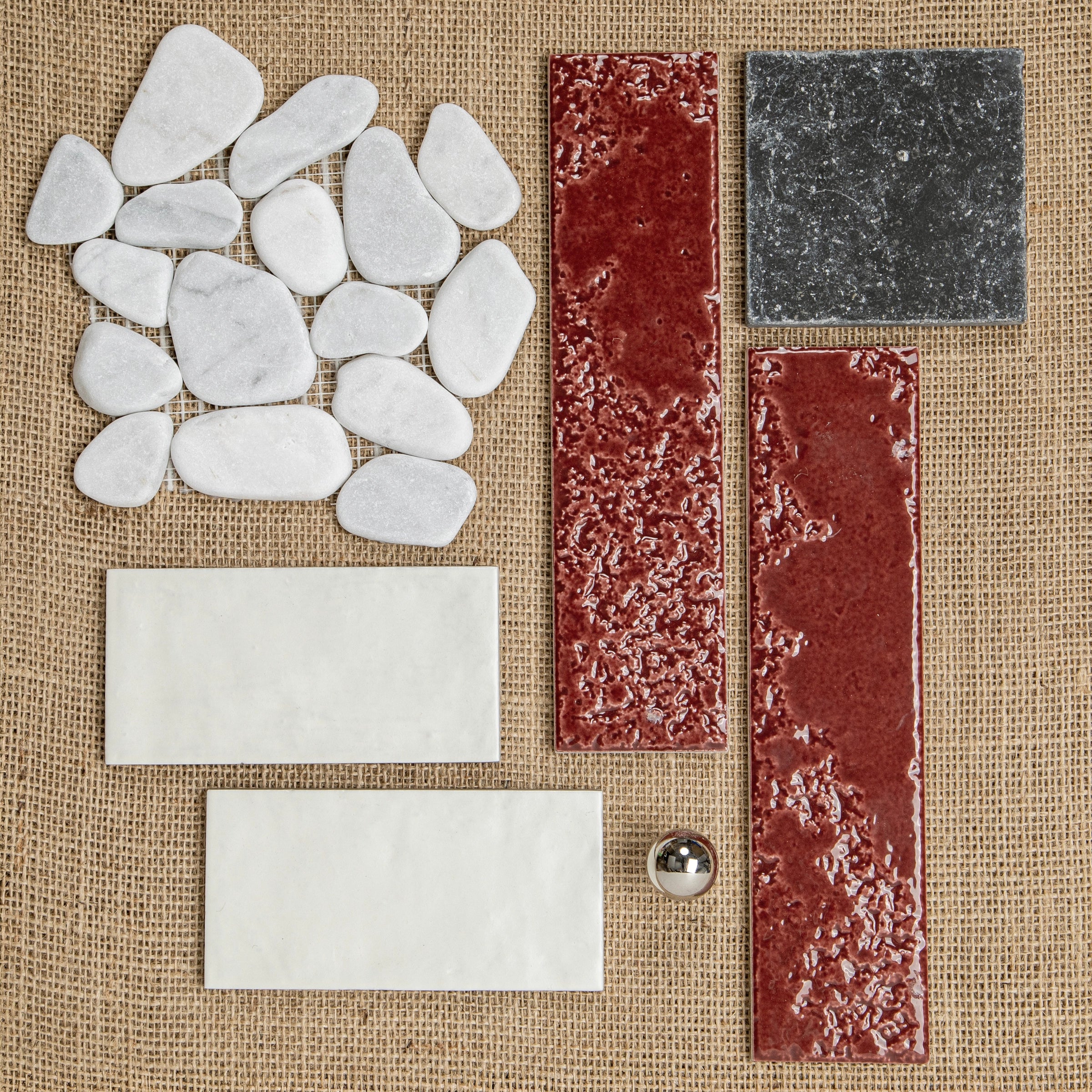 Assorted textured and smooth ceramic and stone tiles in white, deep red, and dark gray arranged on burlap background