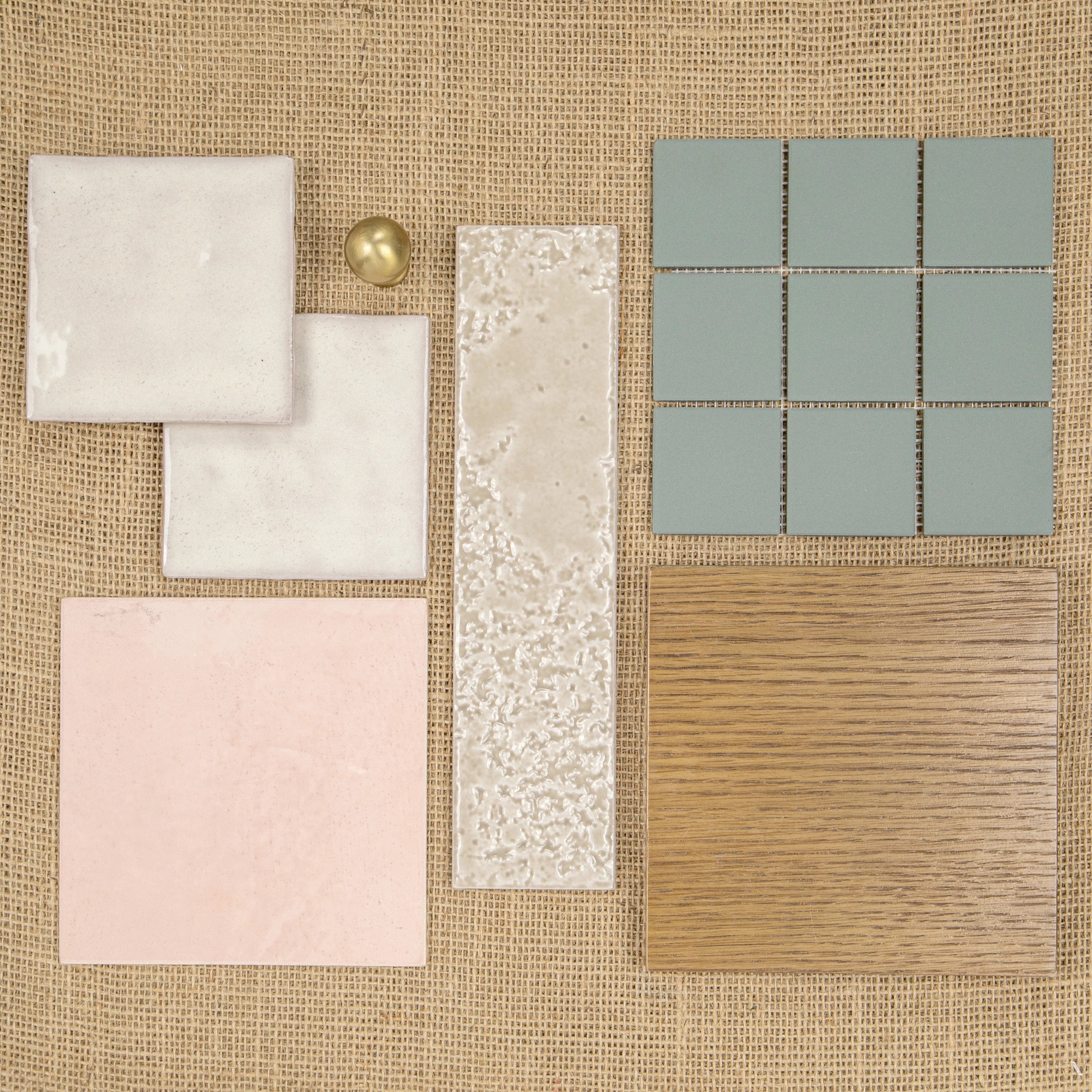 Assorted ceramic tiles in soft pastel shades and wood texture arranged on woven fabric background