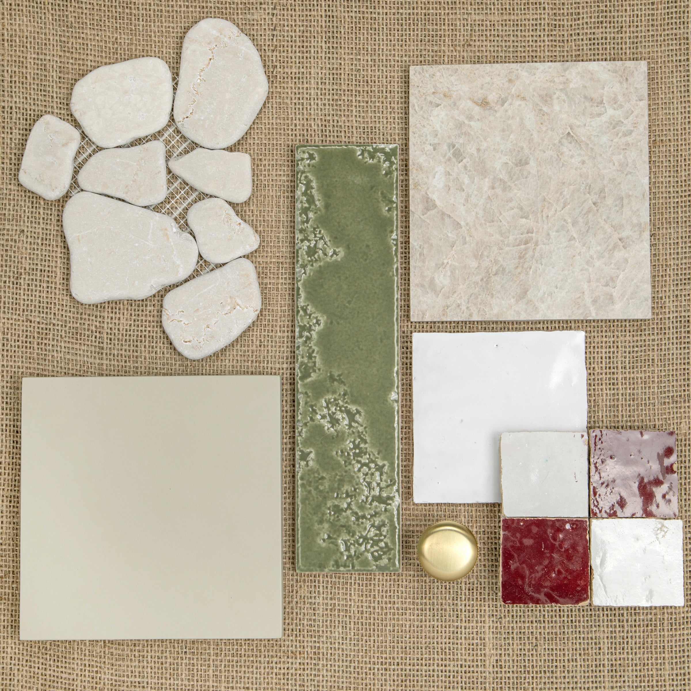 Assortment of ceramic tiles in natural stone, green, cream, white, and deep red shades on textured fabric background
