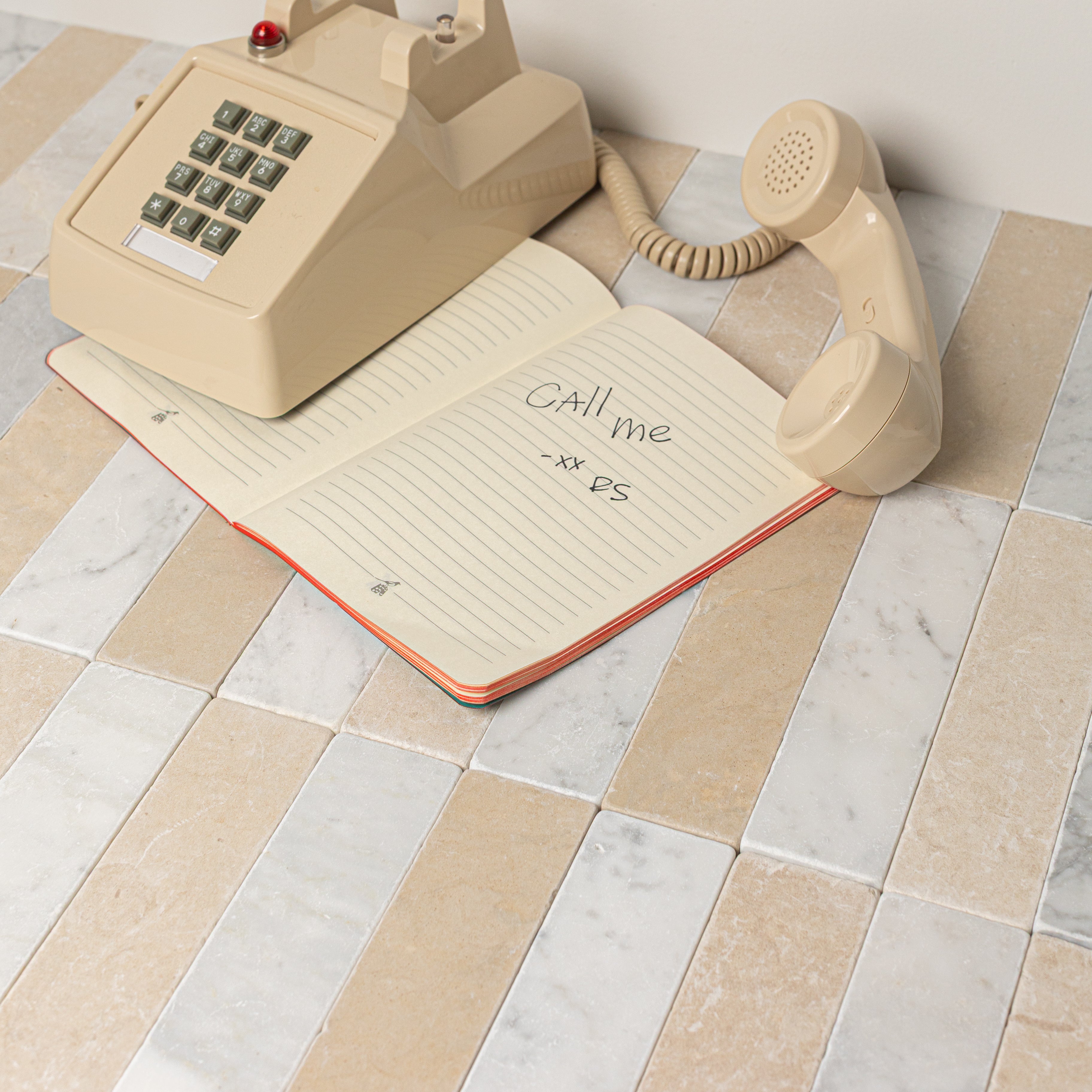 Beige and white rectangular stone tiles arranged in a staggered pattern with a vintage beige rotary phone and notebook nearby