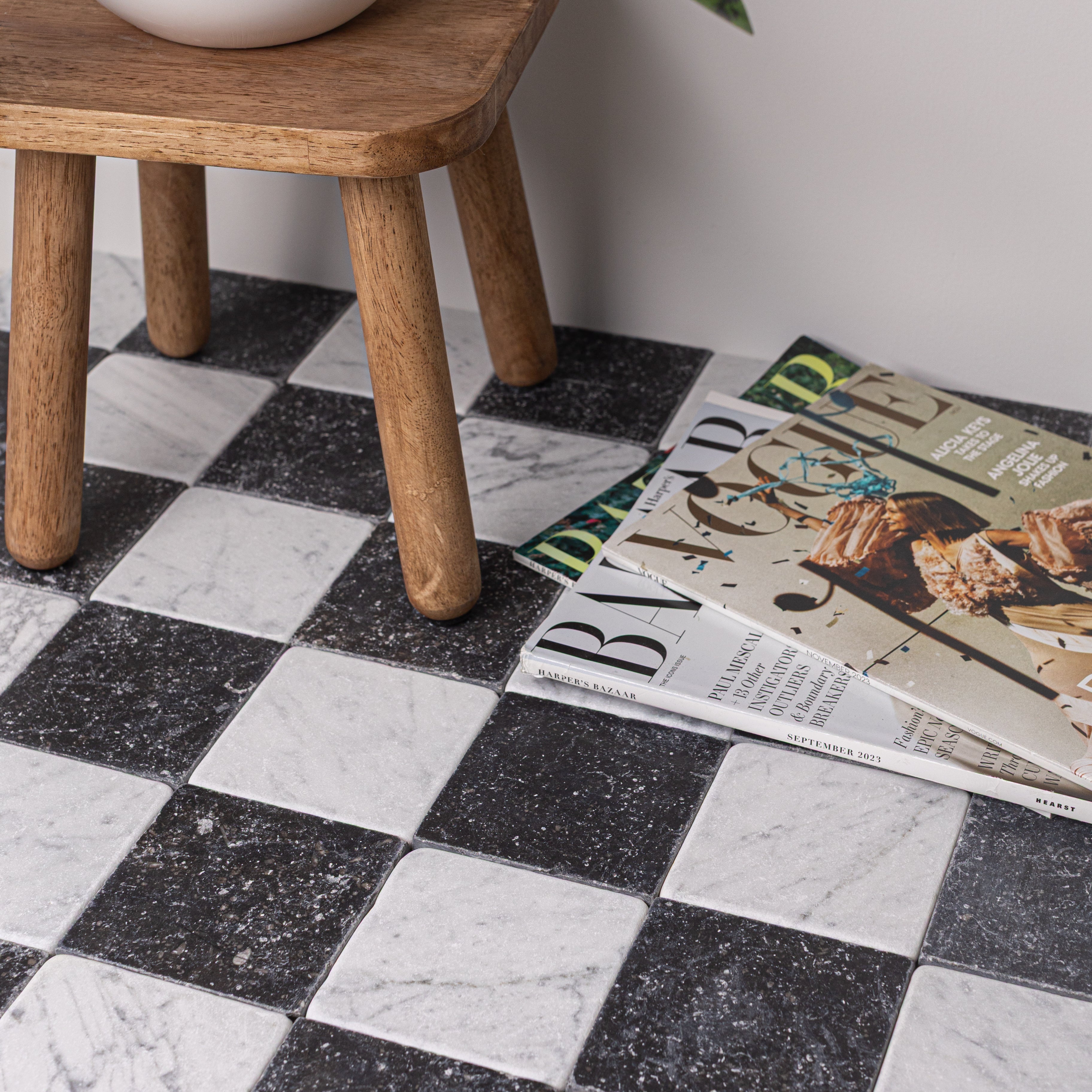 Black and white tumbled stone checkerboard floor with wooden stool legs and stacked lifestyle magazines nearby