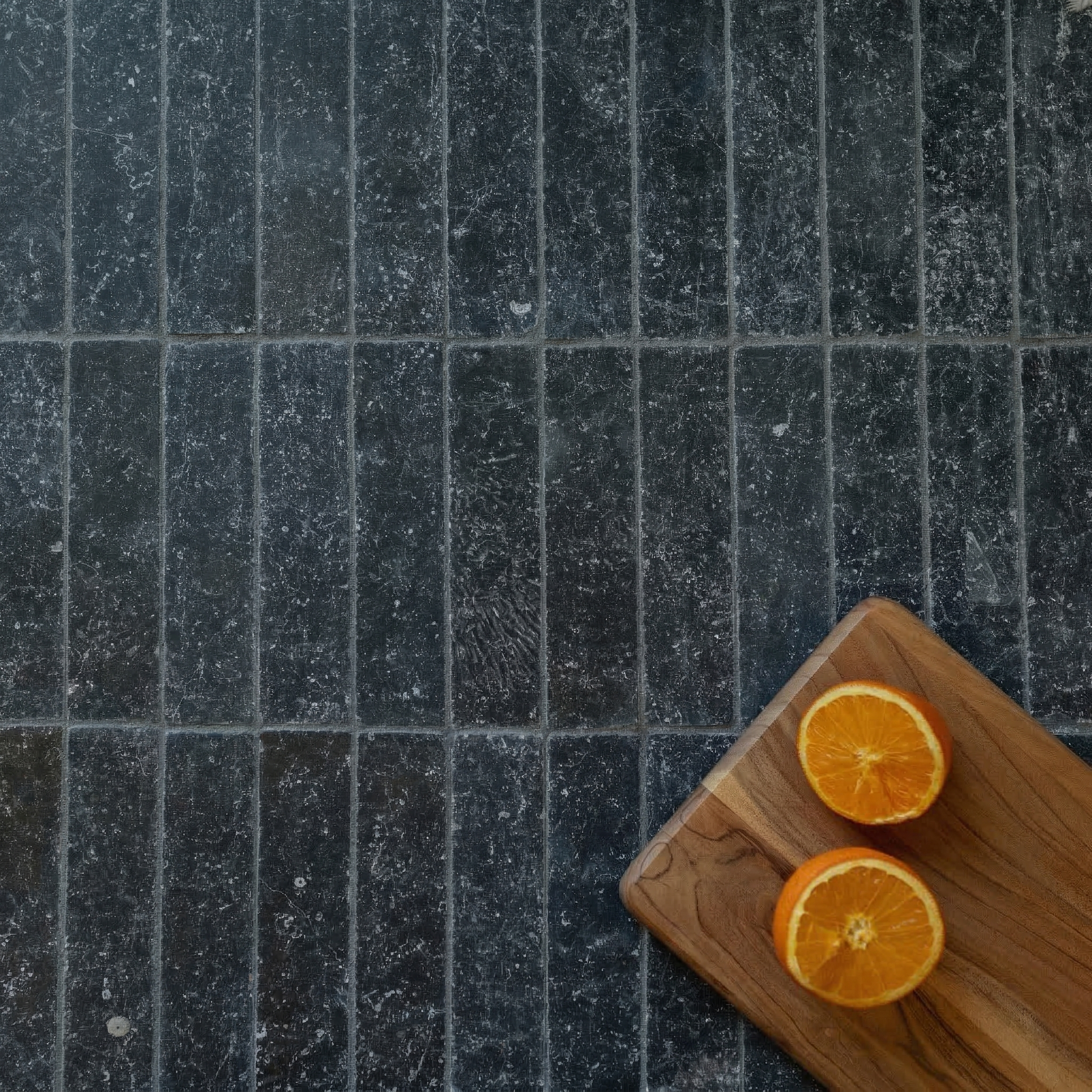 Narrow rectangular blue-gray stone tiles with natural texture arranged beneath a wooden board holding halved oranges